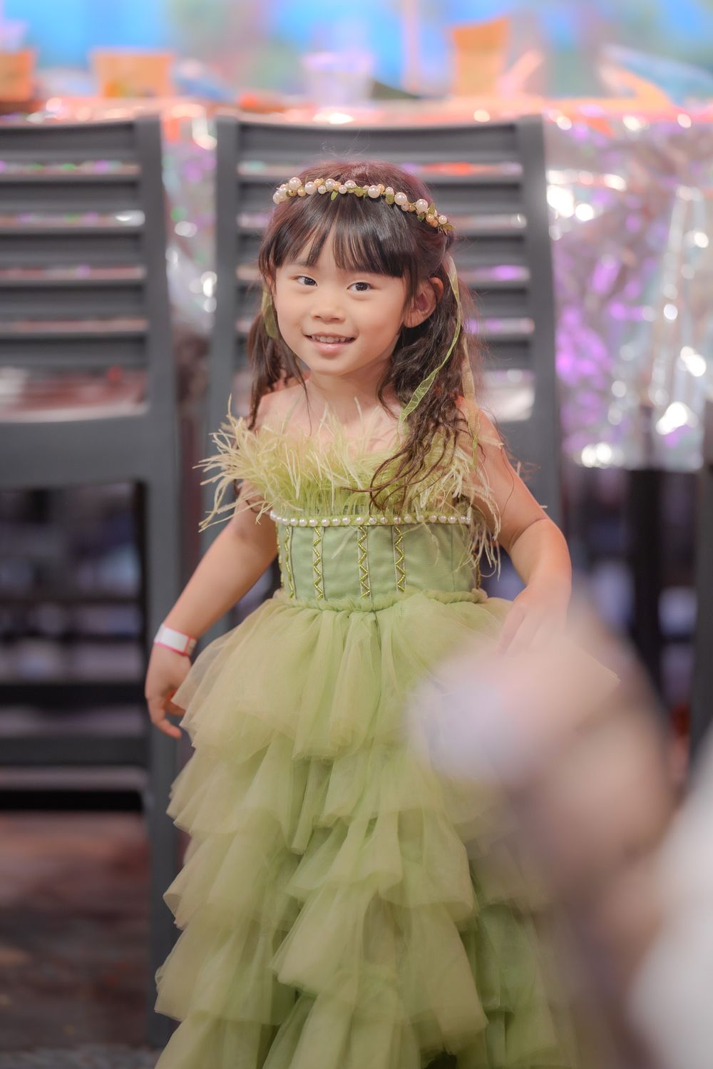 Young girl in a ruffled light green tulle dress smiles while standing in an indoor setting.