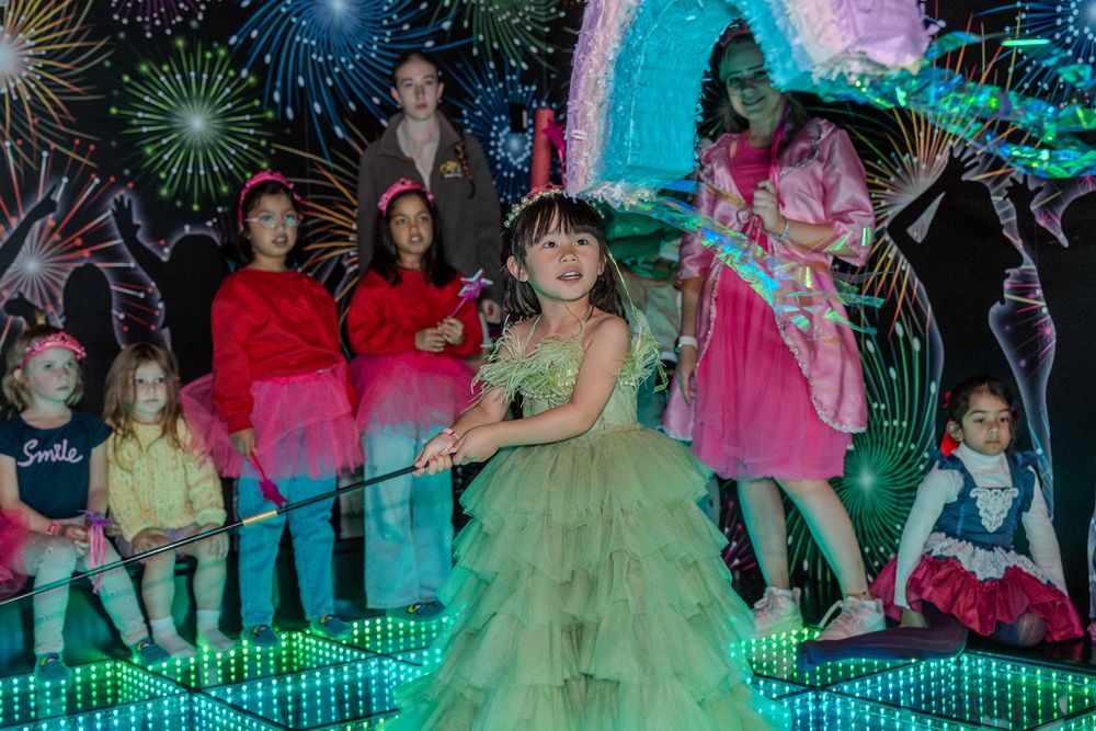Colorful party scene with children in formal attire against neon-lit background with firework designs.