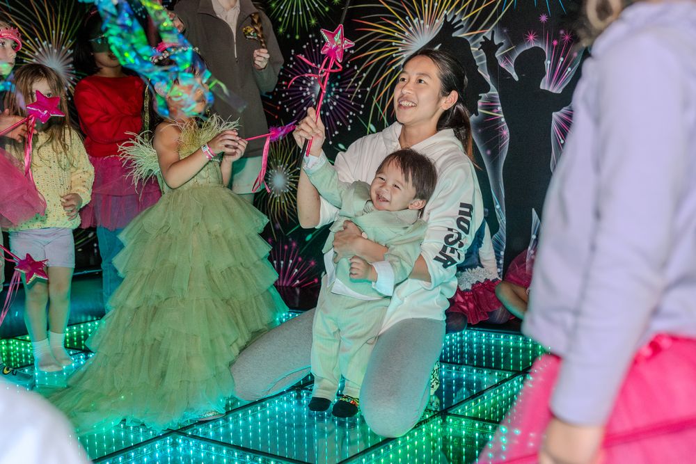 Party guests dance on an illuminated LED floor surrounded by festive decorations at a celebration with colorful lighting.