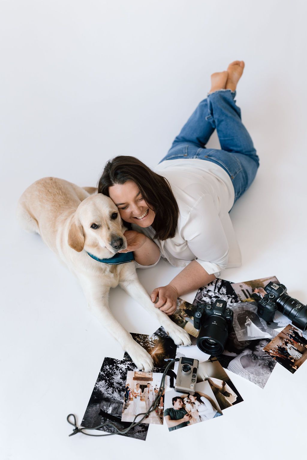 A person lying on white floor with a golden retriever looking at scattered photographs.