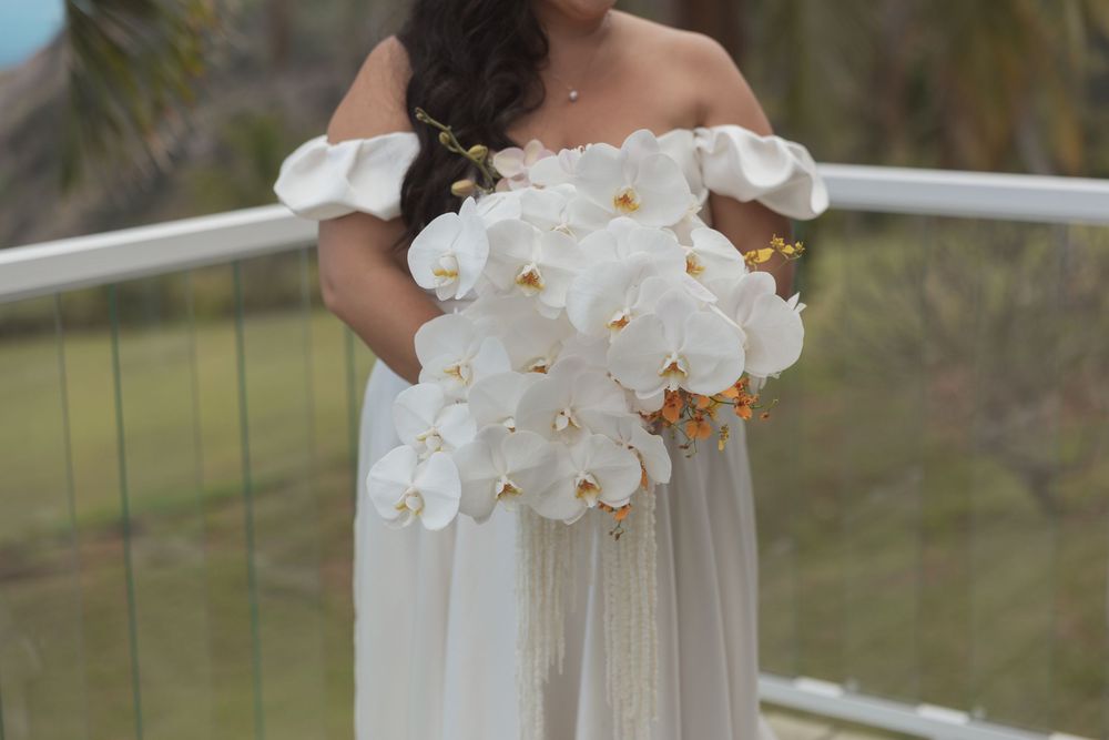 Someone in an off-shoulder white dress holds a stunning bouquet of pure white phalaenopsis orchids.