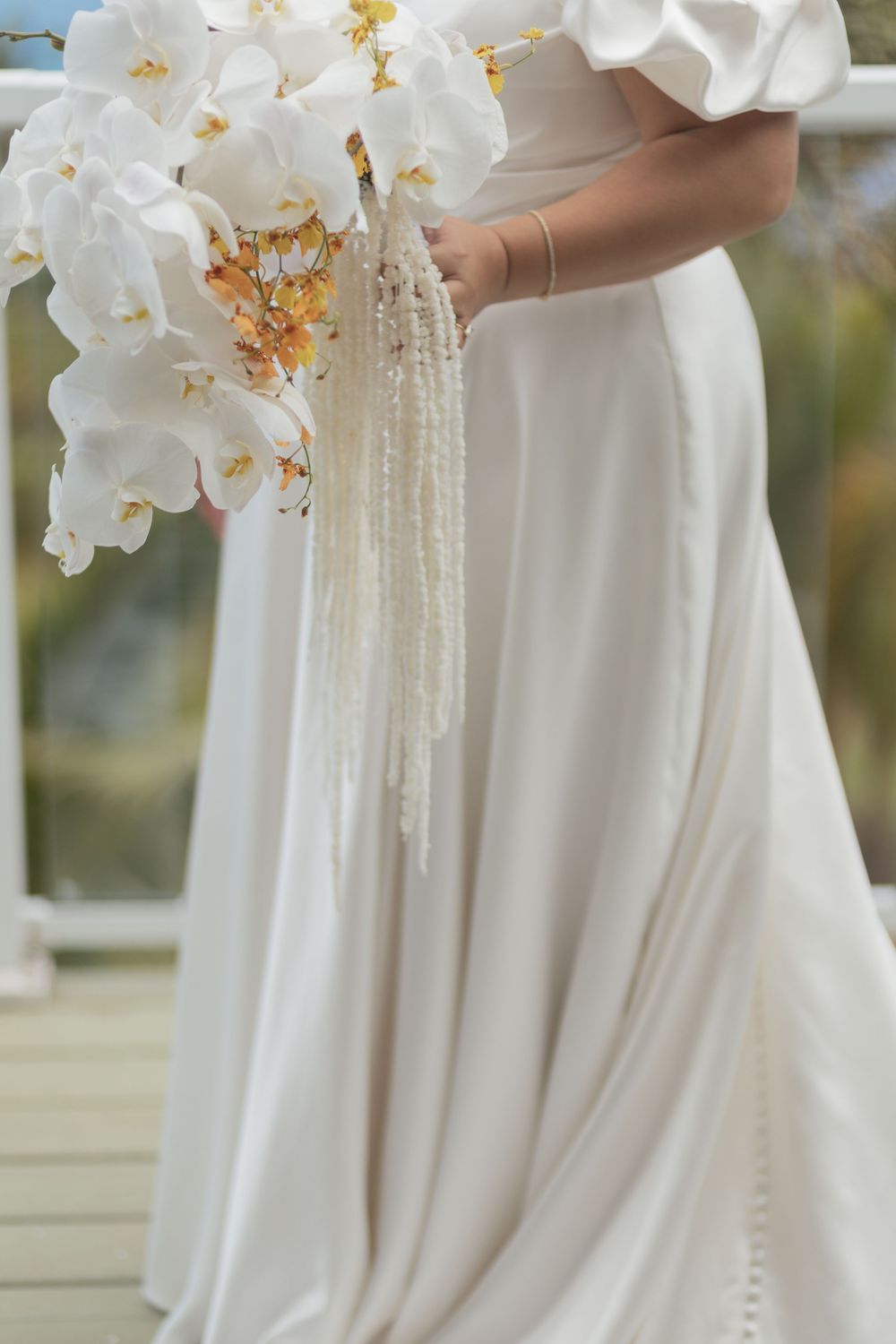 Elegant white orchid bouquet held with cascading pearl strands against a flowing white wedding dress background.