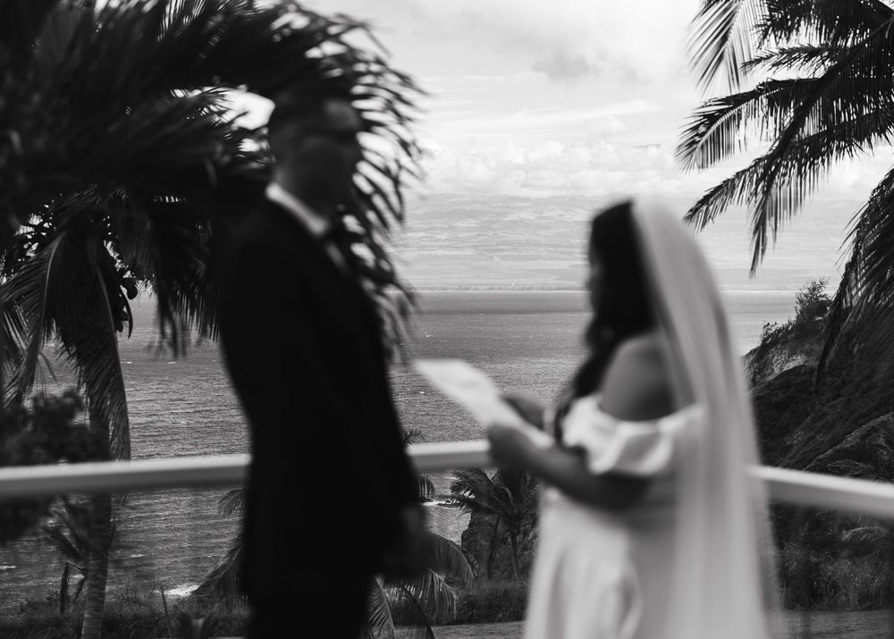 A black and white photo of a couple on a tropical balcony with palm trees and ocean view in the background.