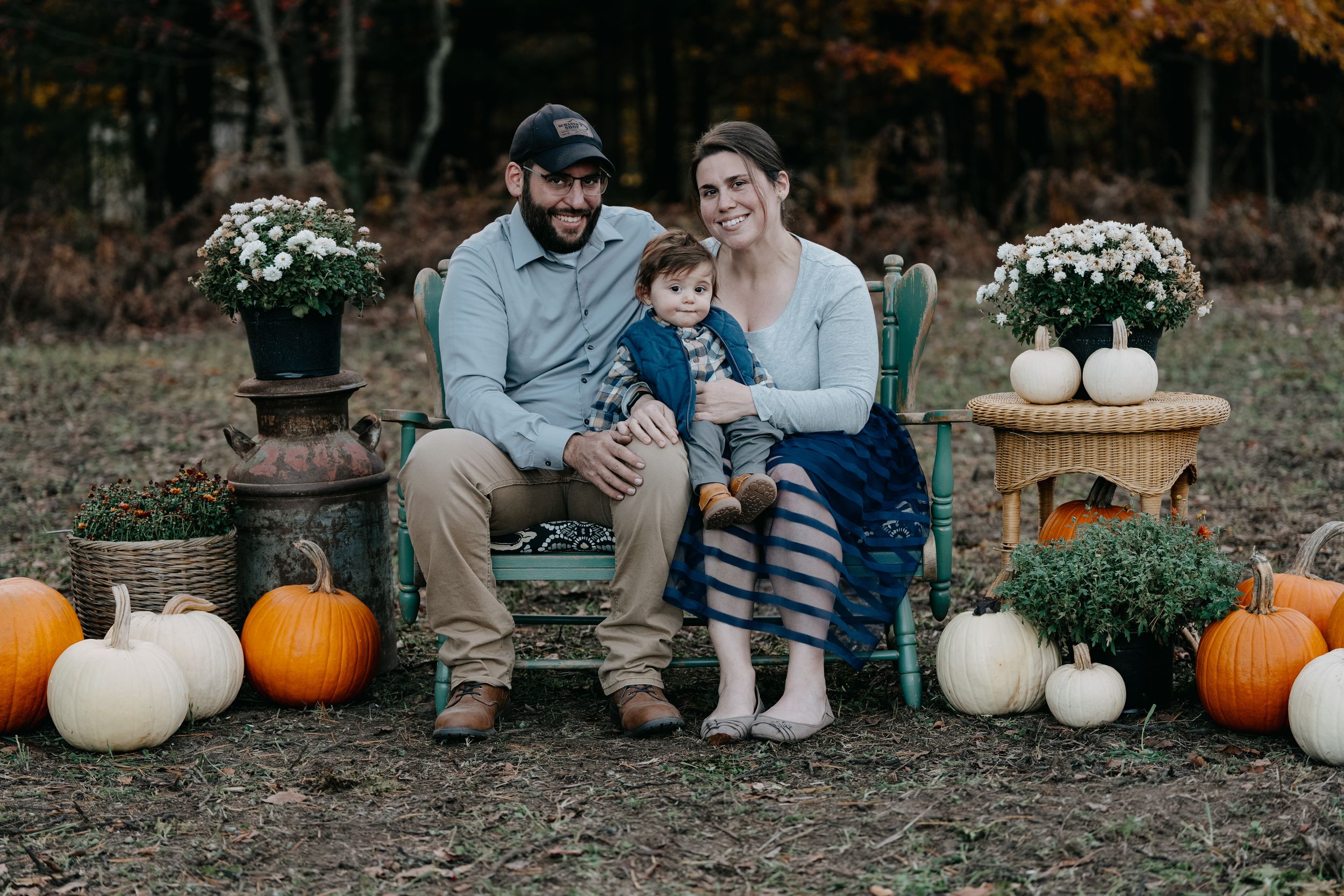 Fall outdoor family photo setup with pumpkins and white mum flowers arranged on wooden crates in a rustic setting.
