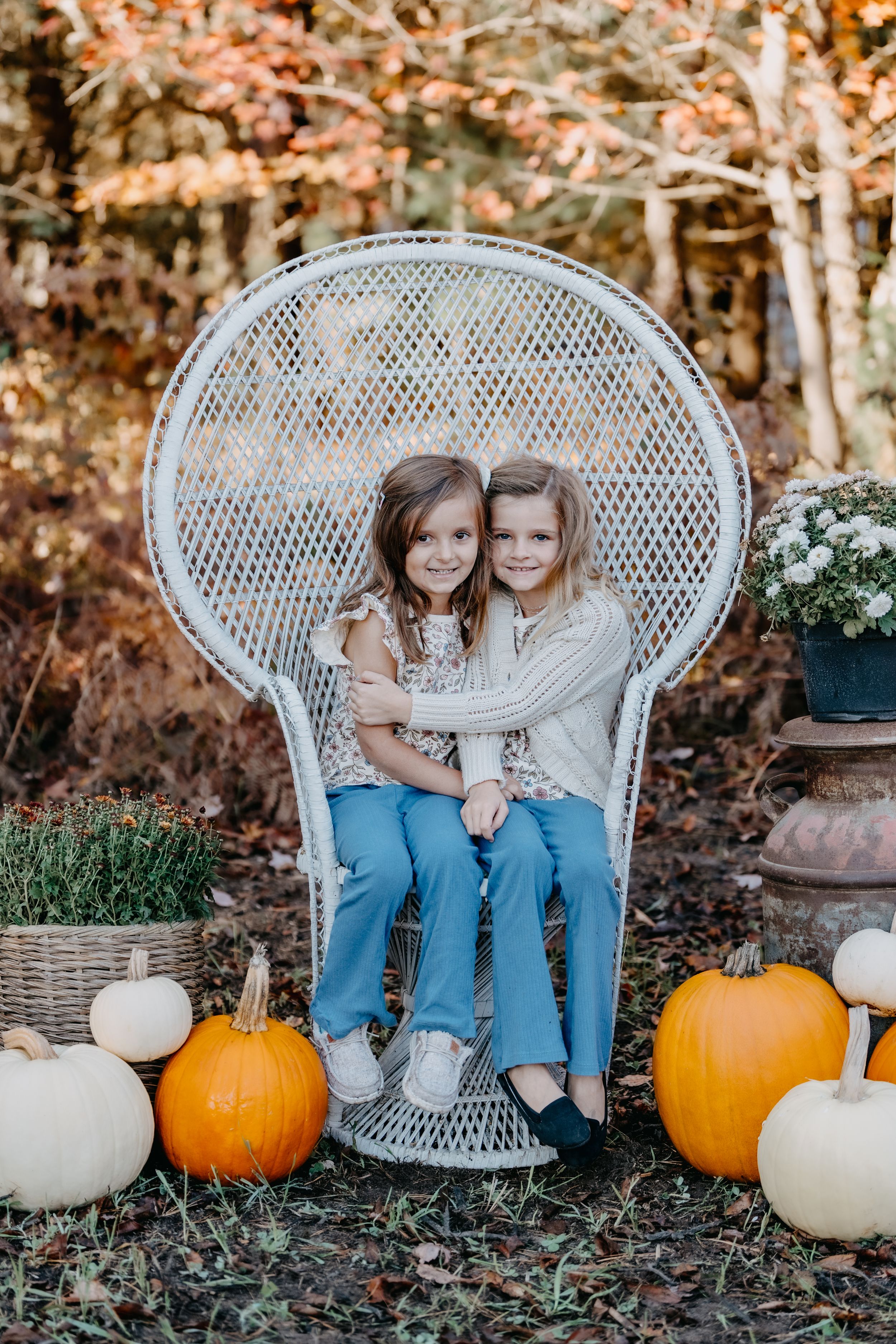 Fall portrait featuring a white wicker peacock chair, seasonal pumpkins and gourds, and autumn foliage in the background.