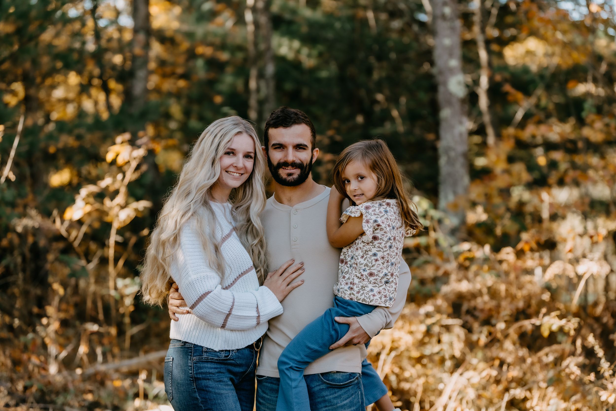 Family enjoying a warm autumn day together in a sunlit forest with golden fall foliage in the background.