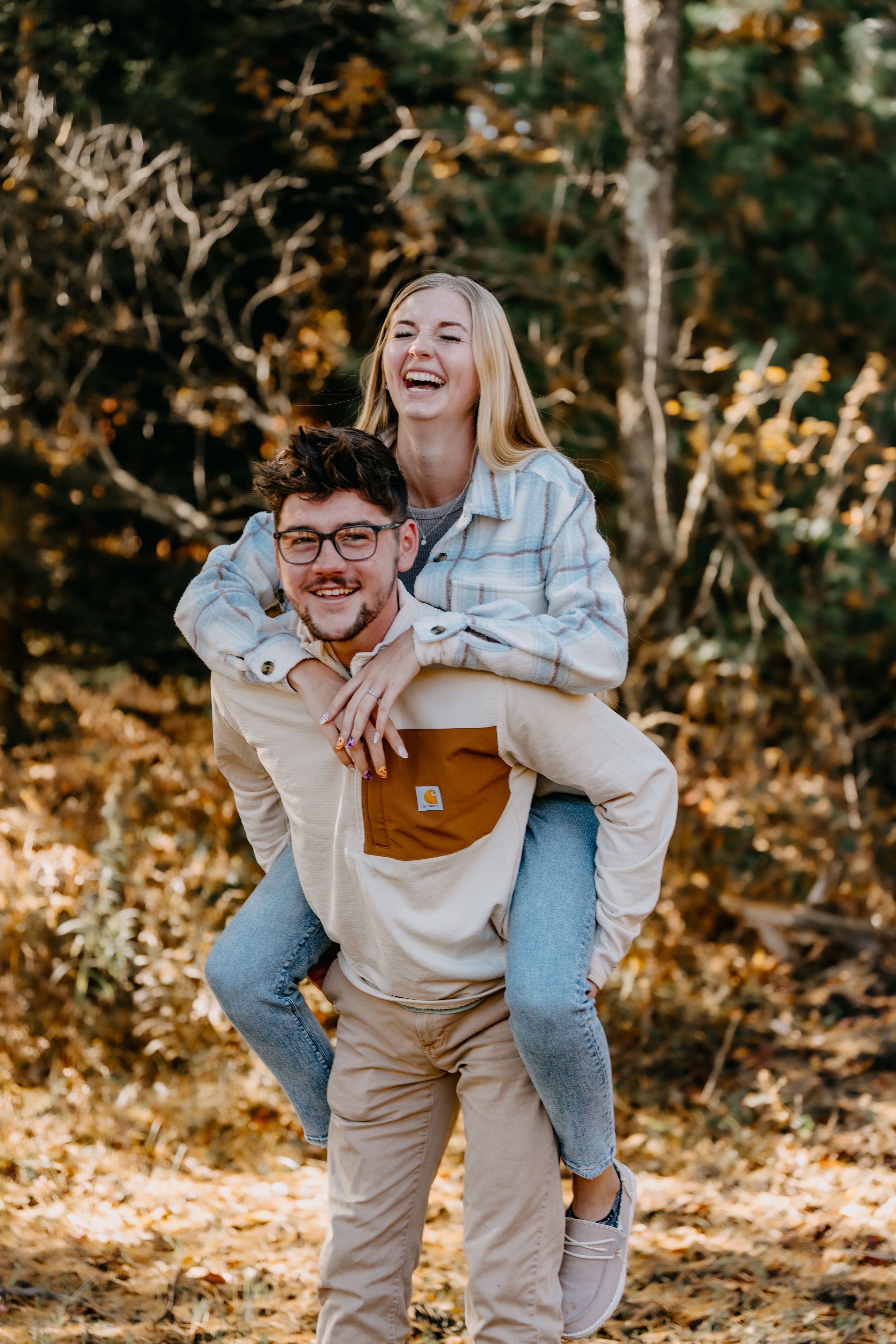 A joyful couple shares a playful piggyback ride moment together in an autumn forest setting.