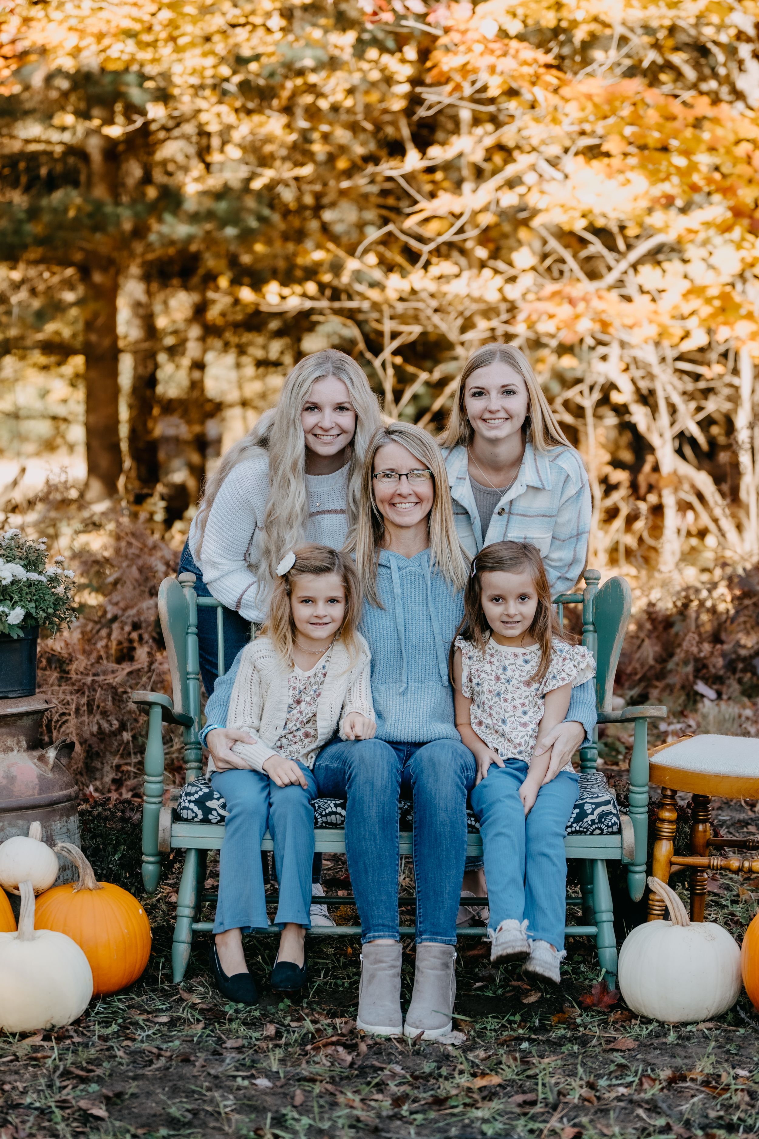 Fall portrait with decorative pumpkins and gourds arranged around a rustic blue bench in an autumn forest setting.