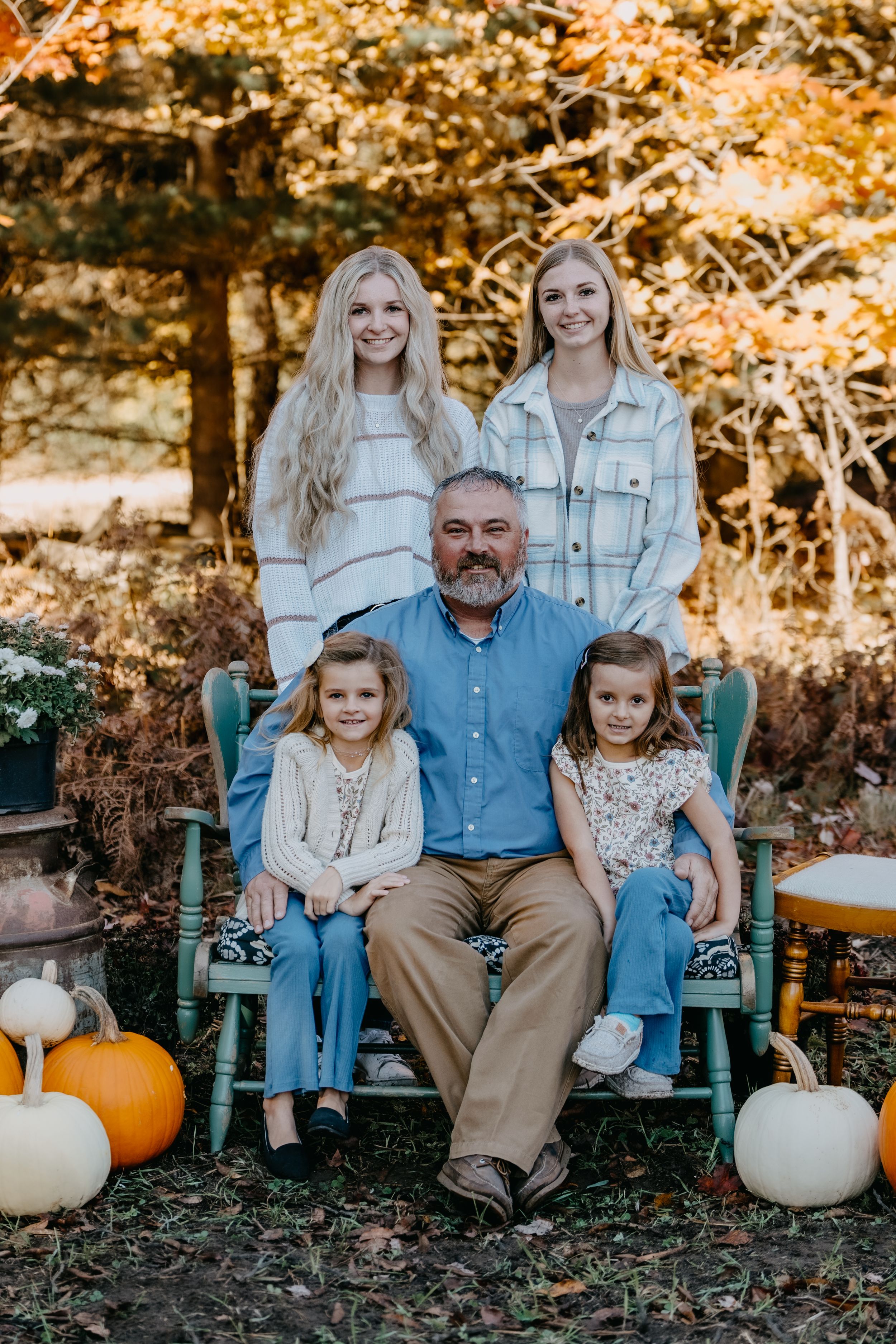 Family autumn portrait on teal bench with pumpkins in golden fall foliage setting.