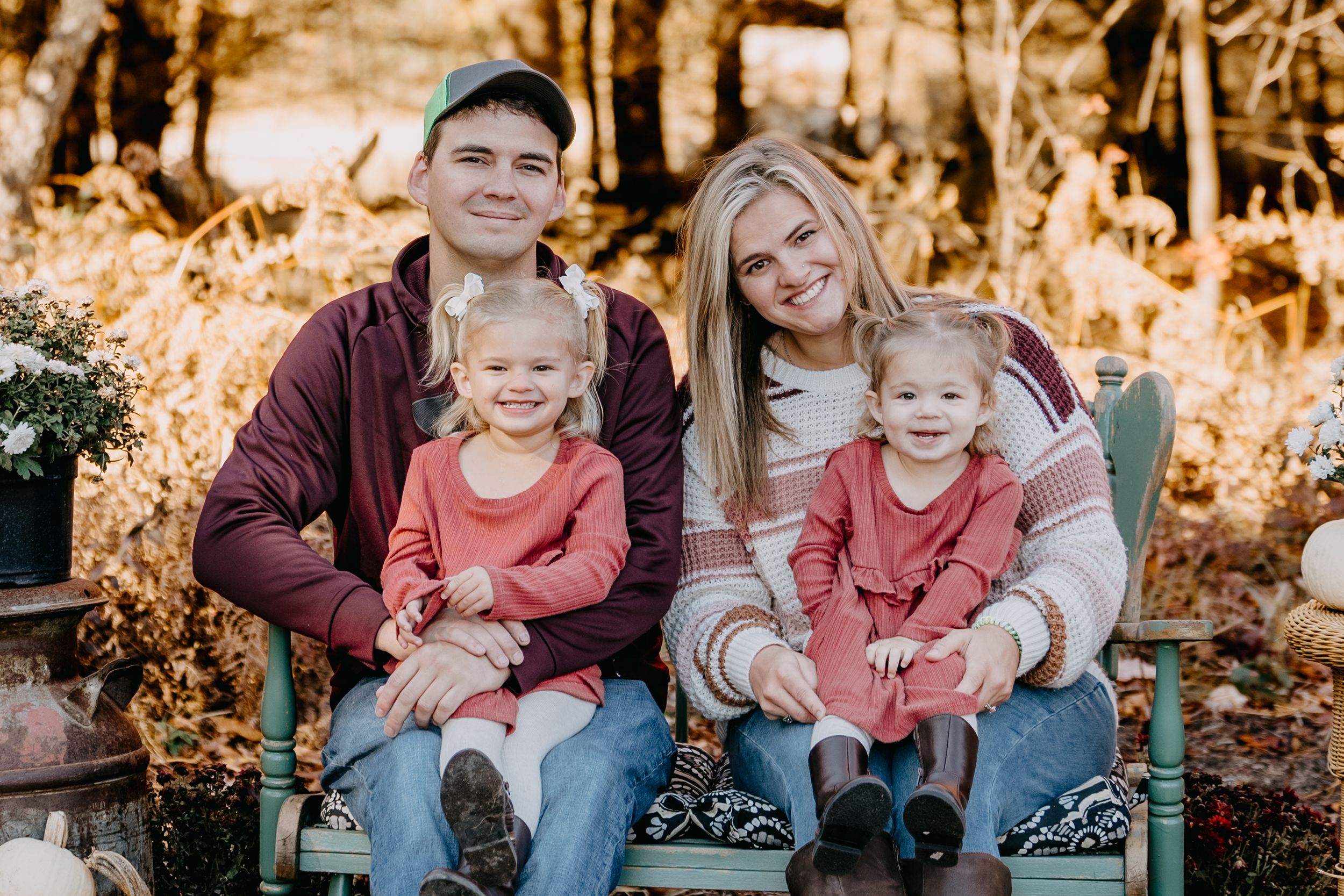 Family in casual clothing sits together on rustic steps during autumn with fall foliage in background.