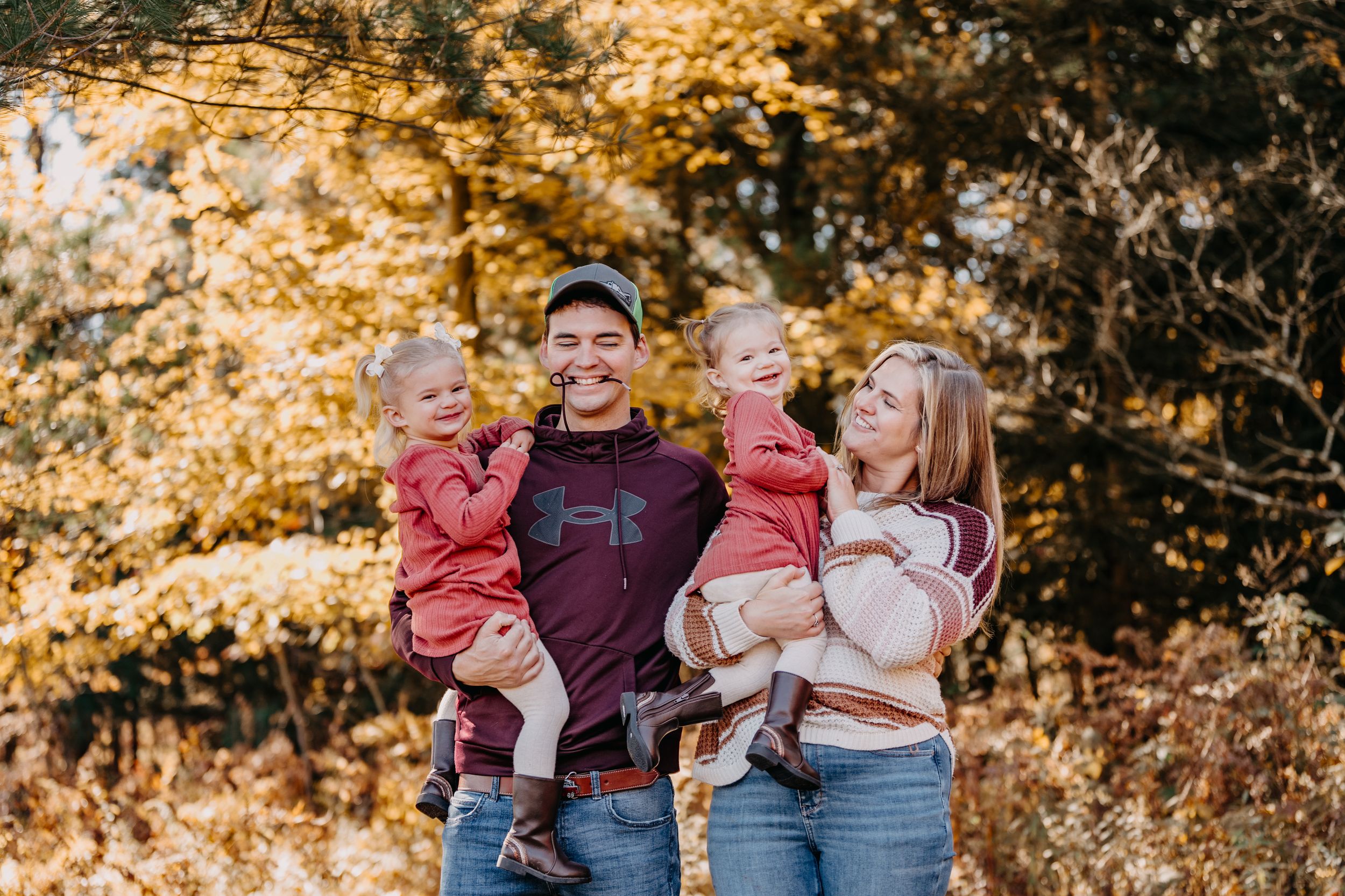 A family poses outdoors in casual clothes with autumn foliage creating a warm golden backdrop in nature.