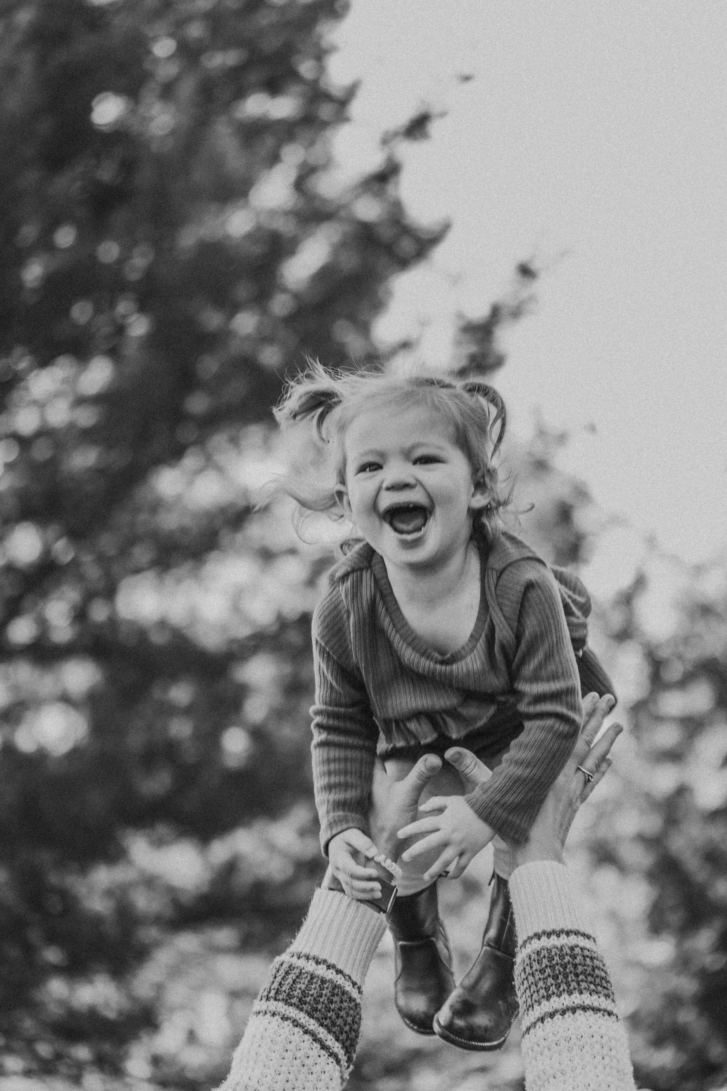 A joyful child being lifted in the air in black and white photography with trees in the background.