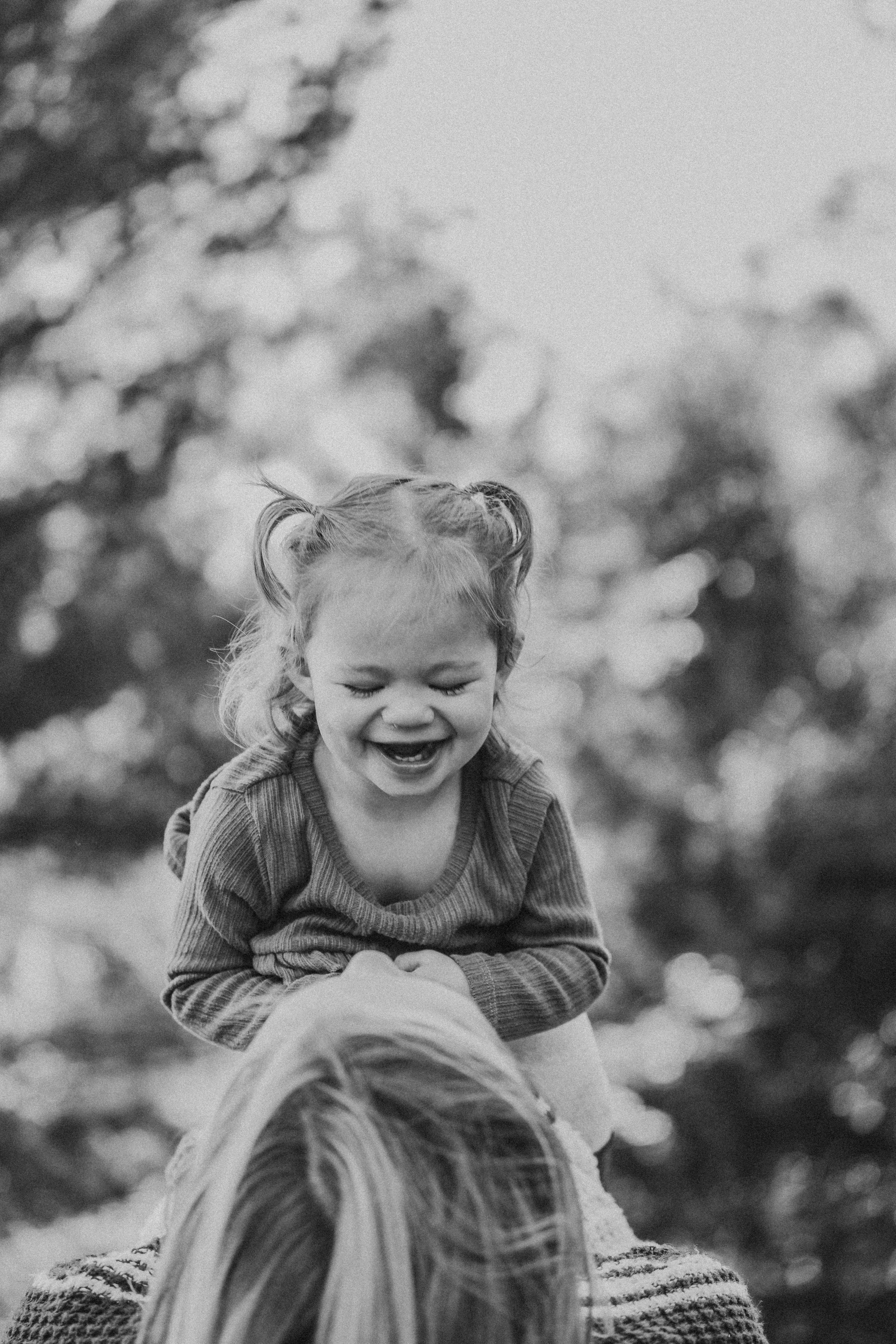 Joyful black and white portrait of a laughing child with pigtails outdoors.