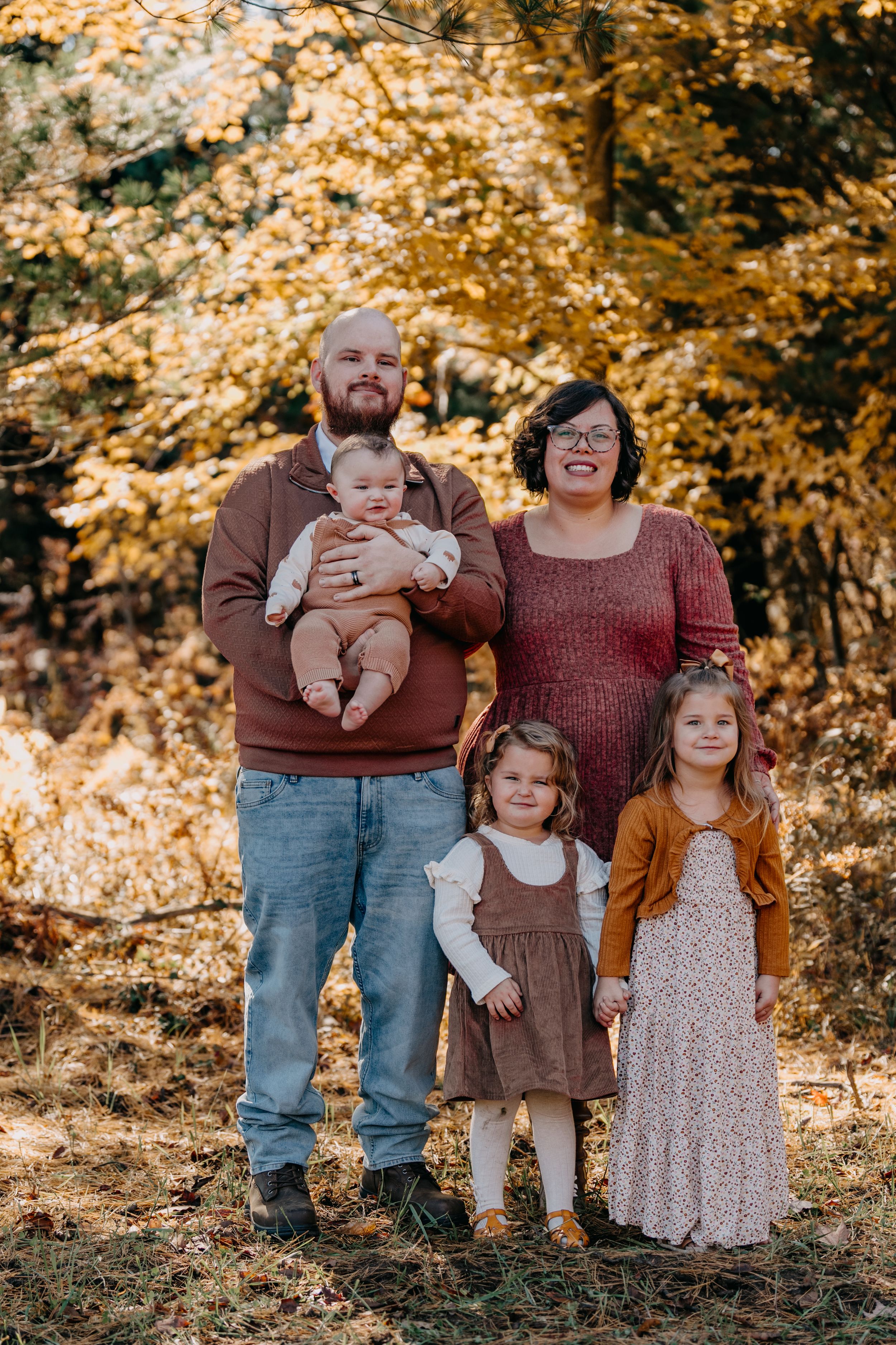 A family poses together in an autumn setting with golden foliage and warm lighting creating a cozy outdoor portrait.