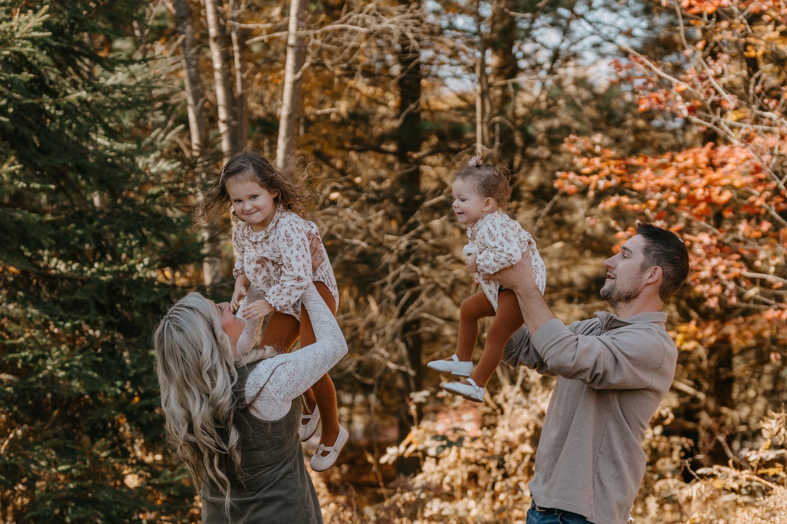 Two parents lifting and playing with children outdoors during autumn with golden foliage in the background.