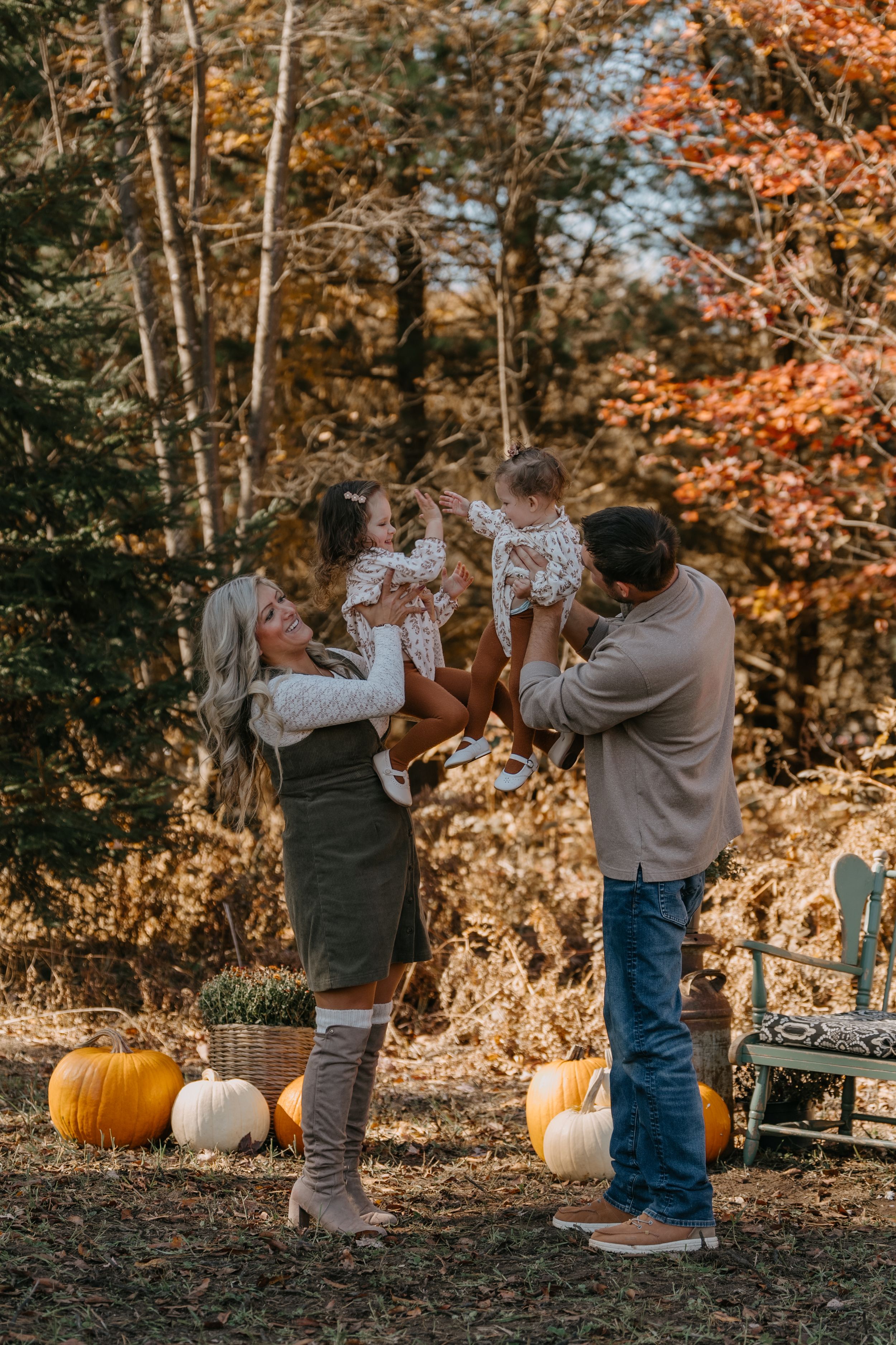 A family poses for autumn photos surrounded by fall foliage and pumpkins on a sunny afternoon.