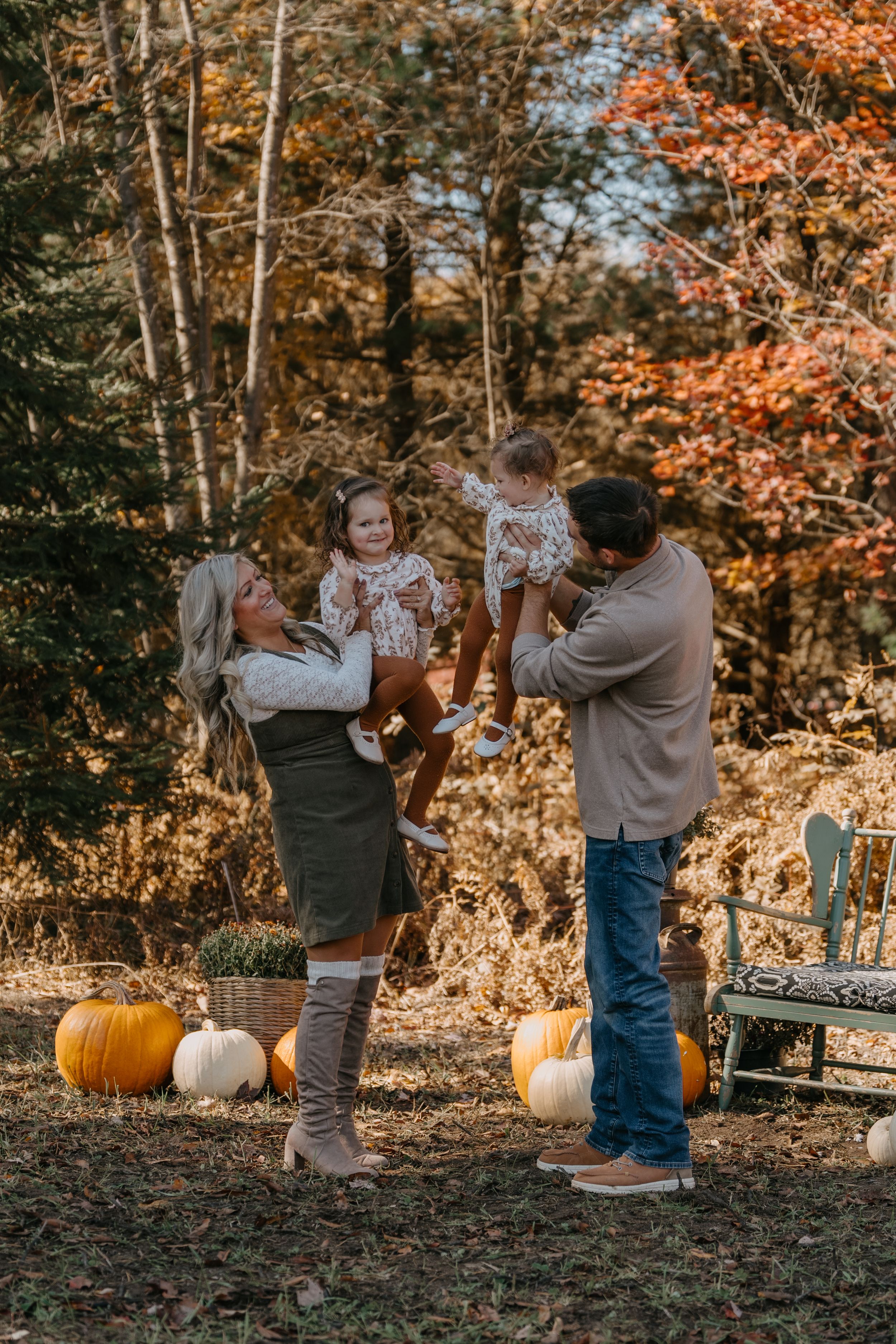 Parents play with their children outdoors during a fall photoshoot with orange leaves and pumpkins.
