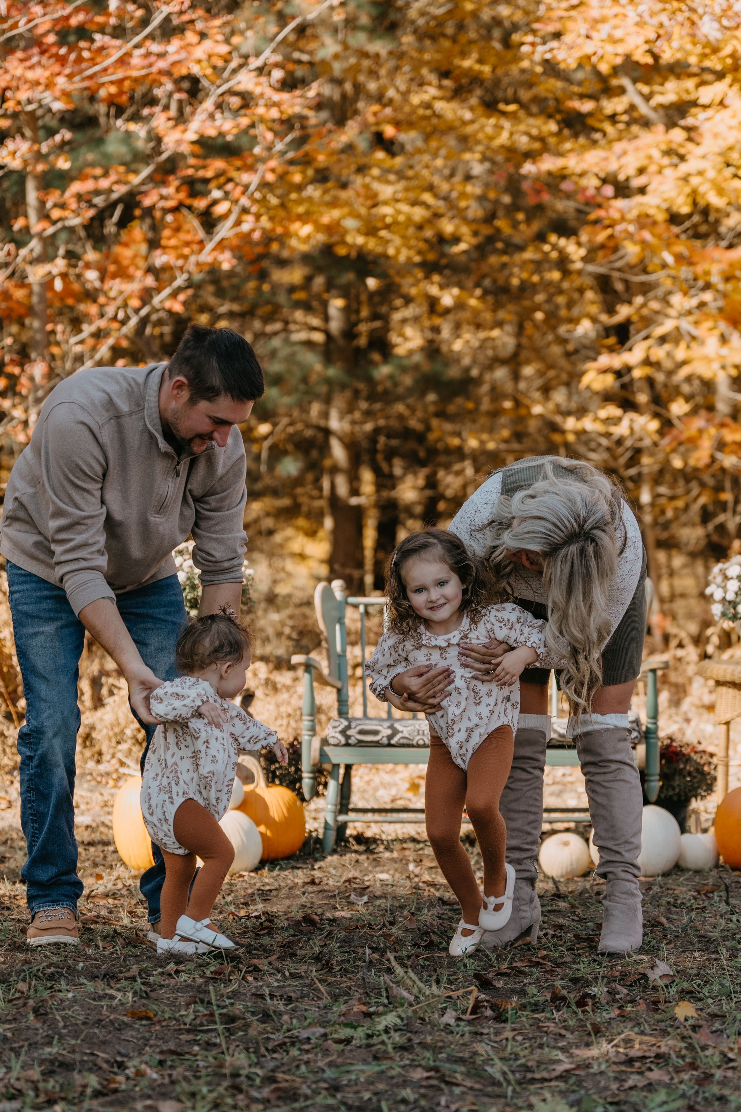 Family enjoying fall activities with pumpkins and decorations in a scenic autumn forest setting.