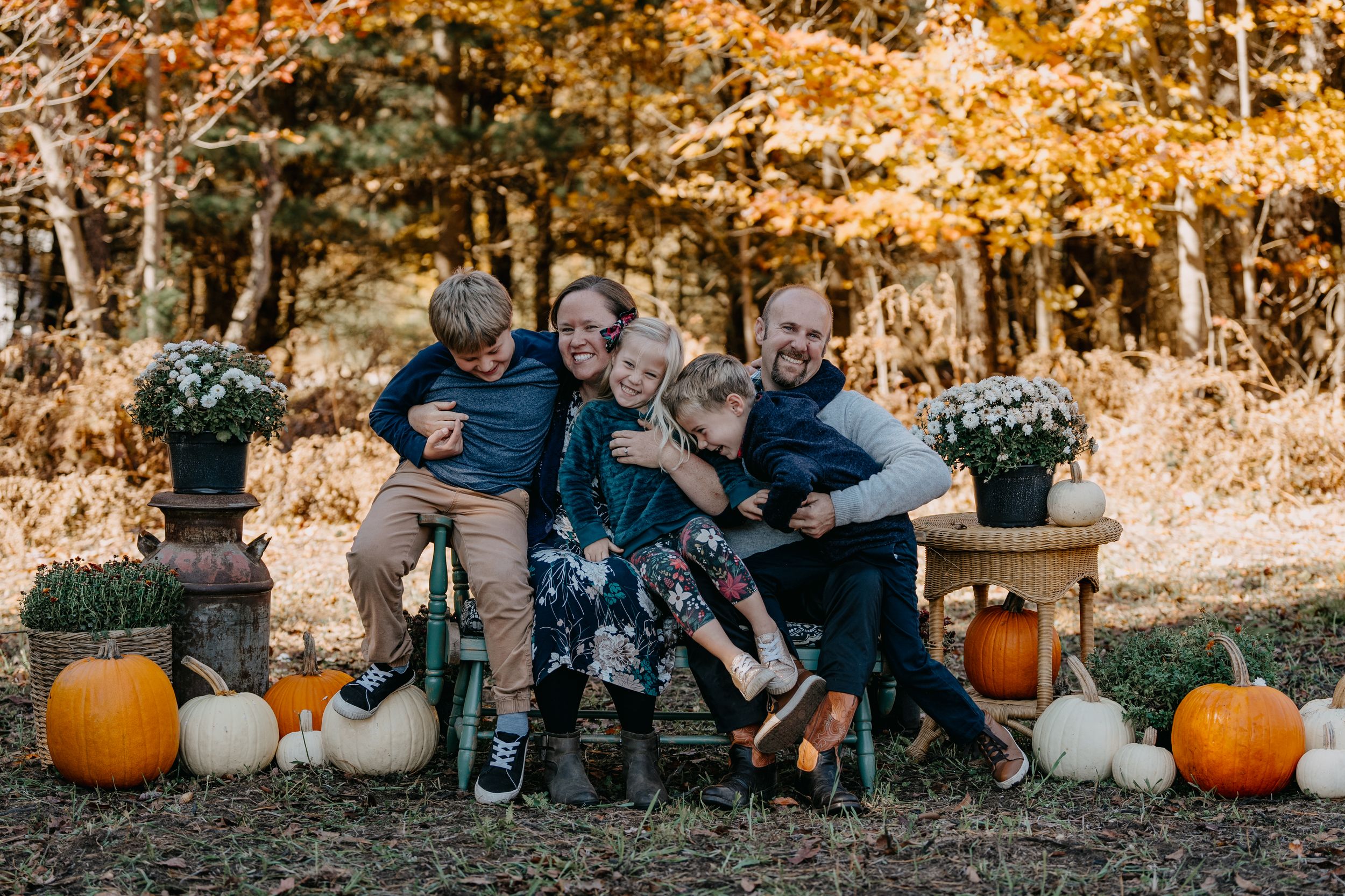 Autumn outdoor scene decorated with white and orange pumpkins and potted flowers around people sitting on rustic bench.