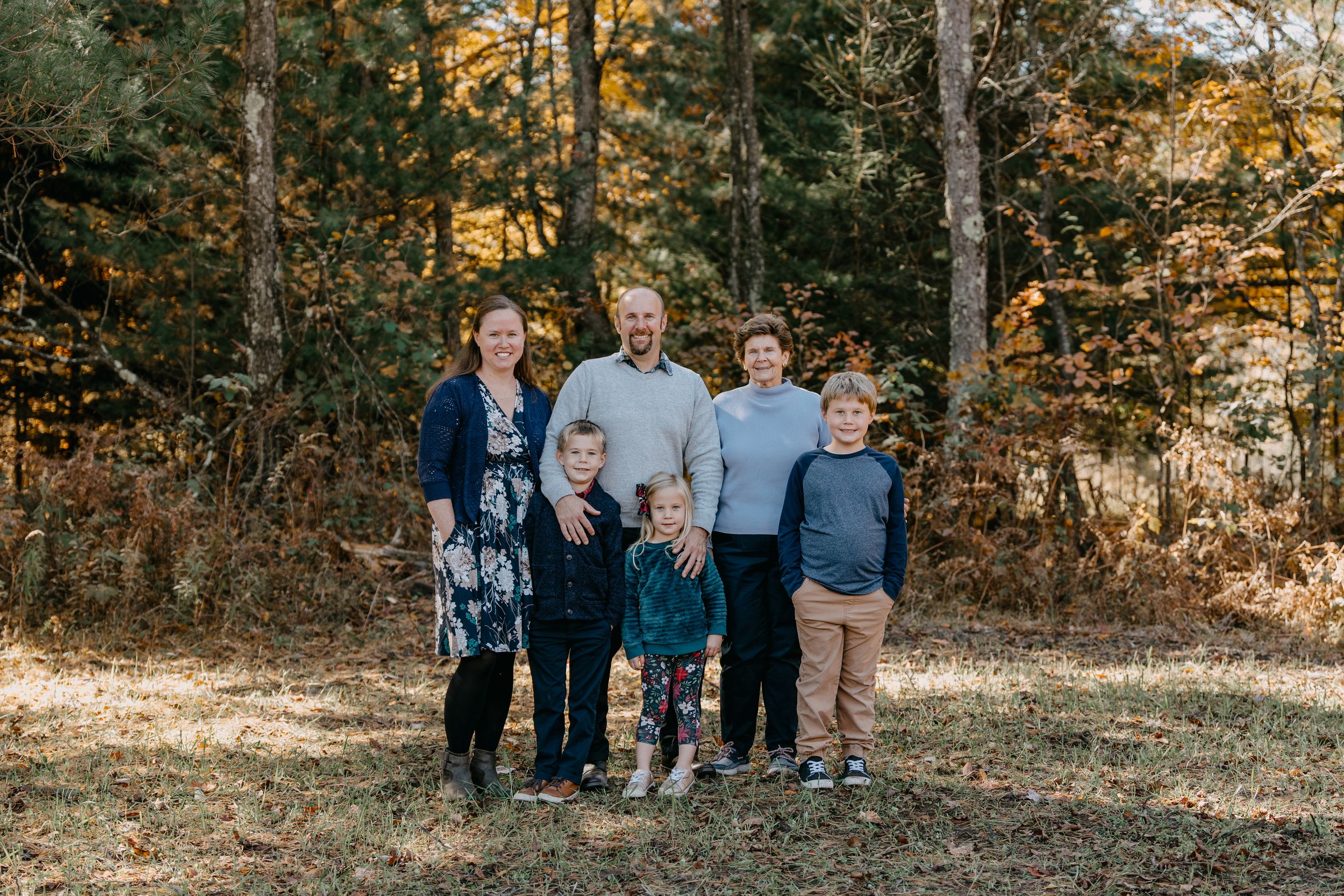Family group standing together outdoors in autumn forest setting during golden hour photo session.