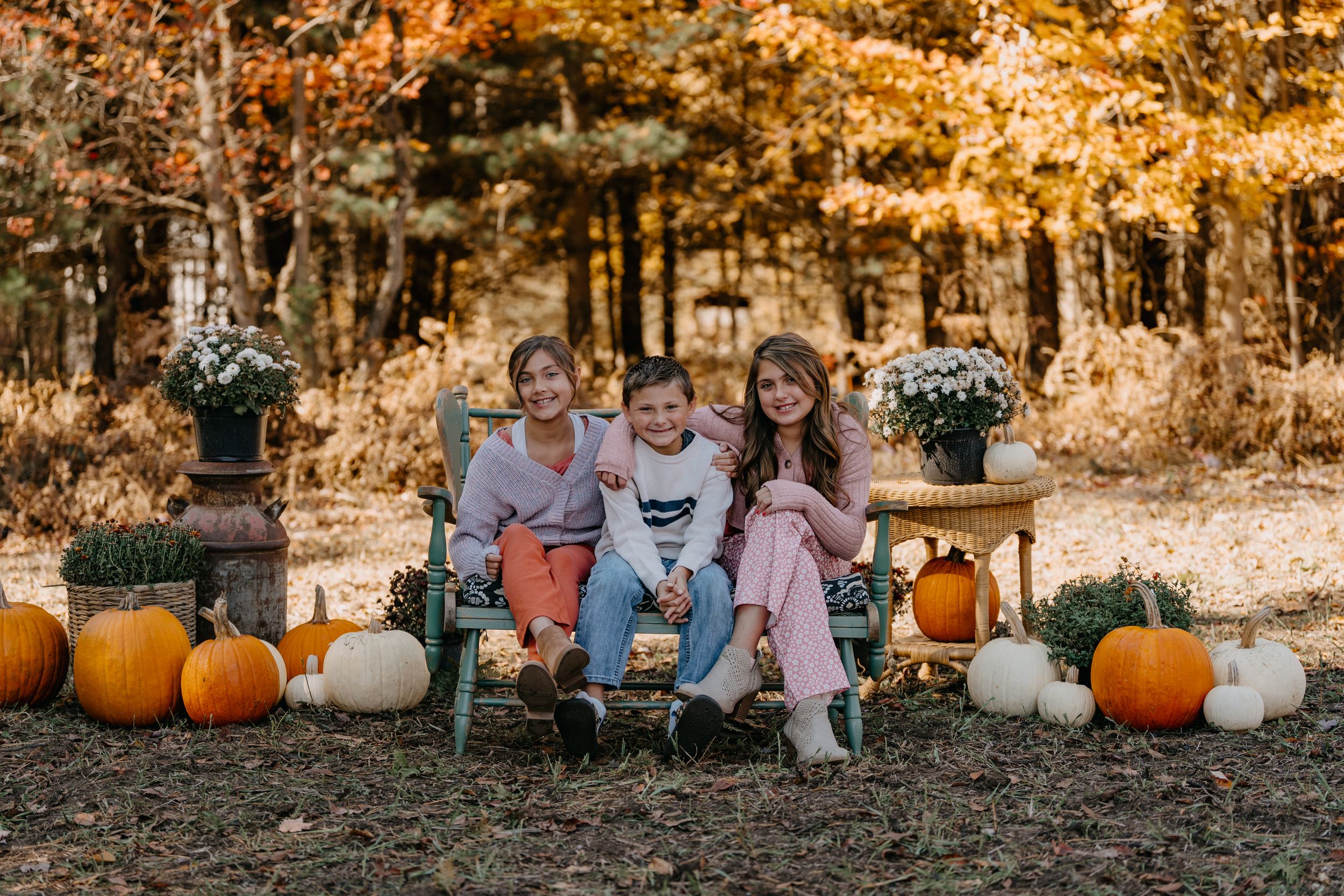Fall family photo session with pumpkins and warm golden sunlight filtering through autumn trees in a park setting.