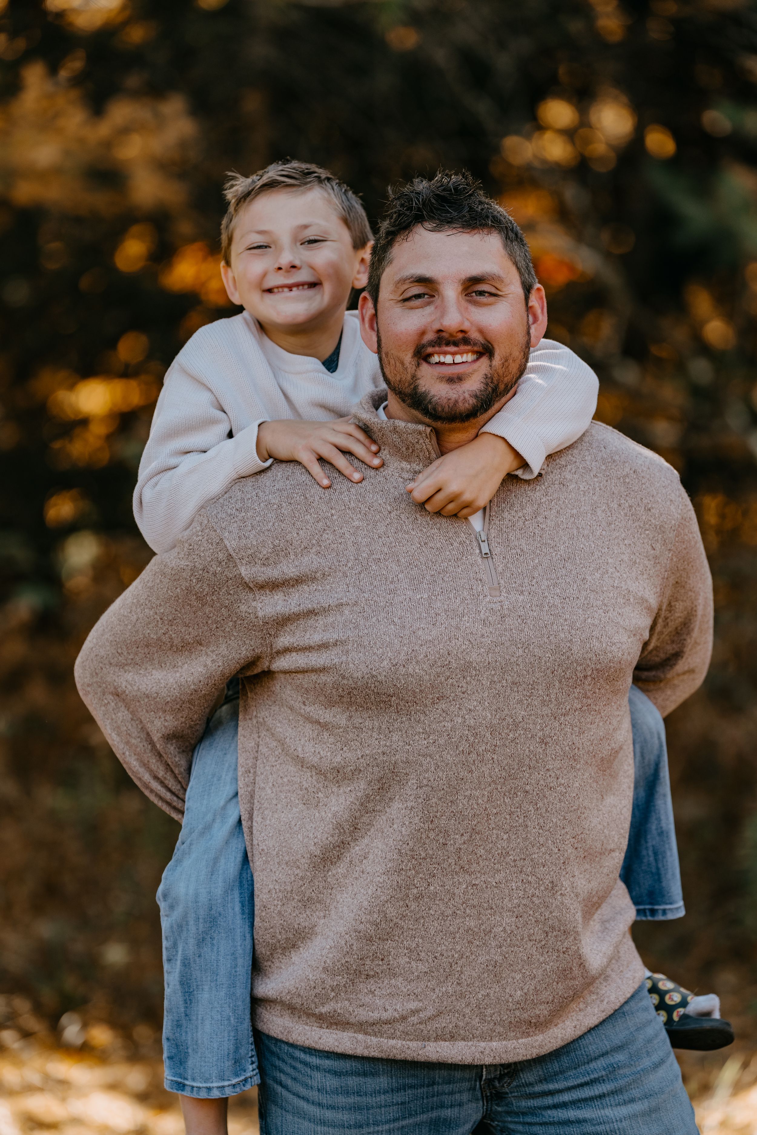 A parent and child share a warm embrace outdoors, both wearing cozy sweaters on an autumn day.