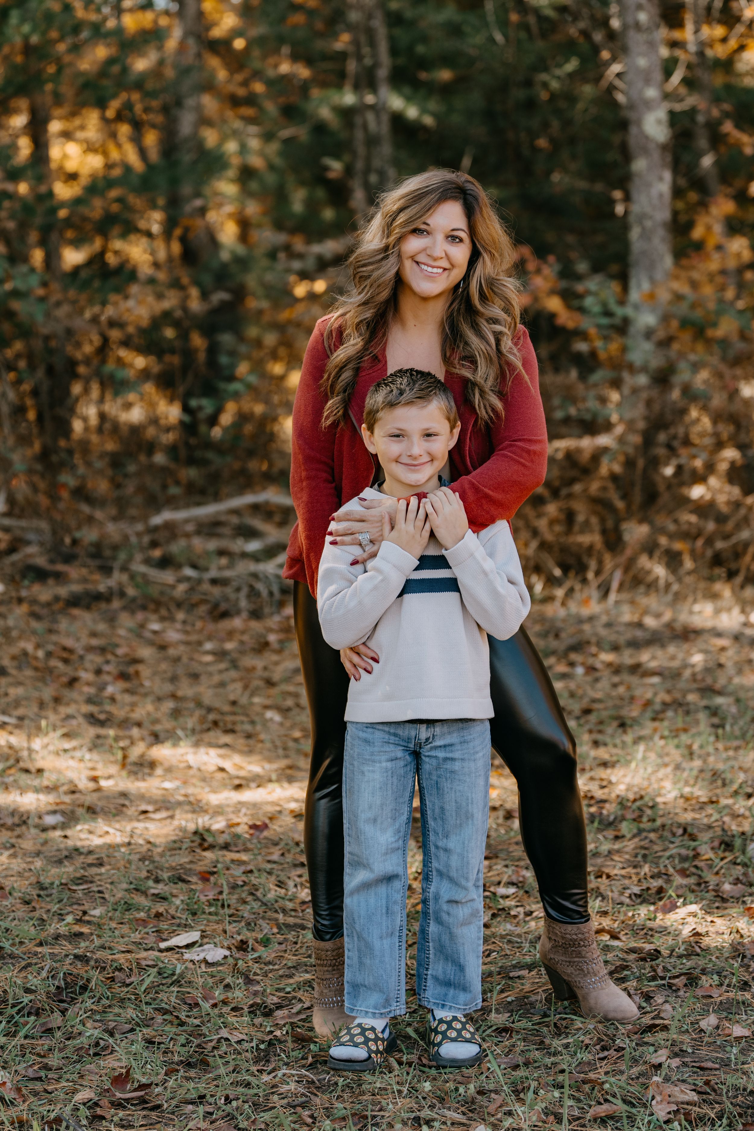 A tender outdoor autumn scene of a parent and child in casual wear sharing a warm embrace in a wooded setting.