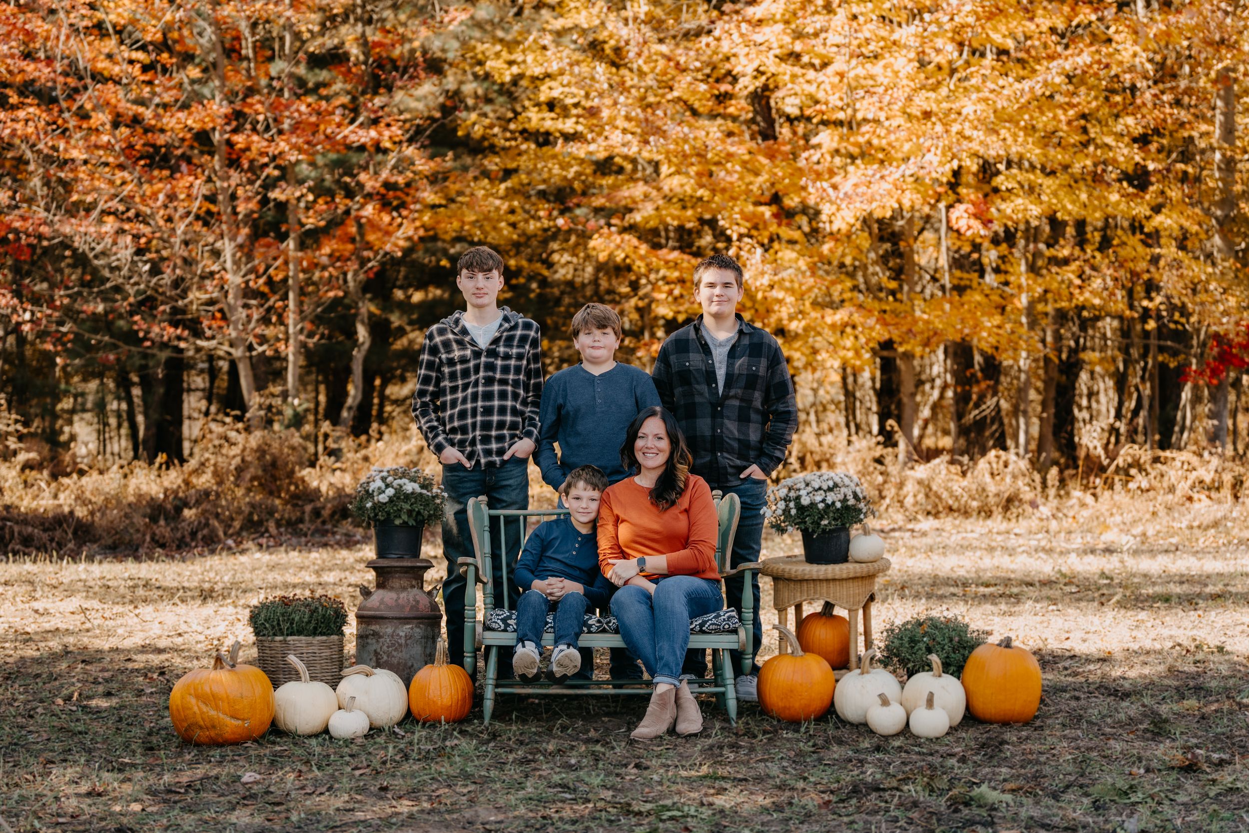 Fall family photo session with rustic bench seating and decorative pumpkins against backdrop of golden autumn foliage.