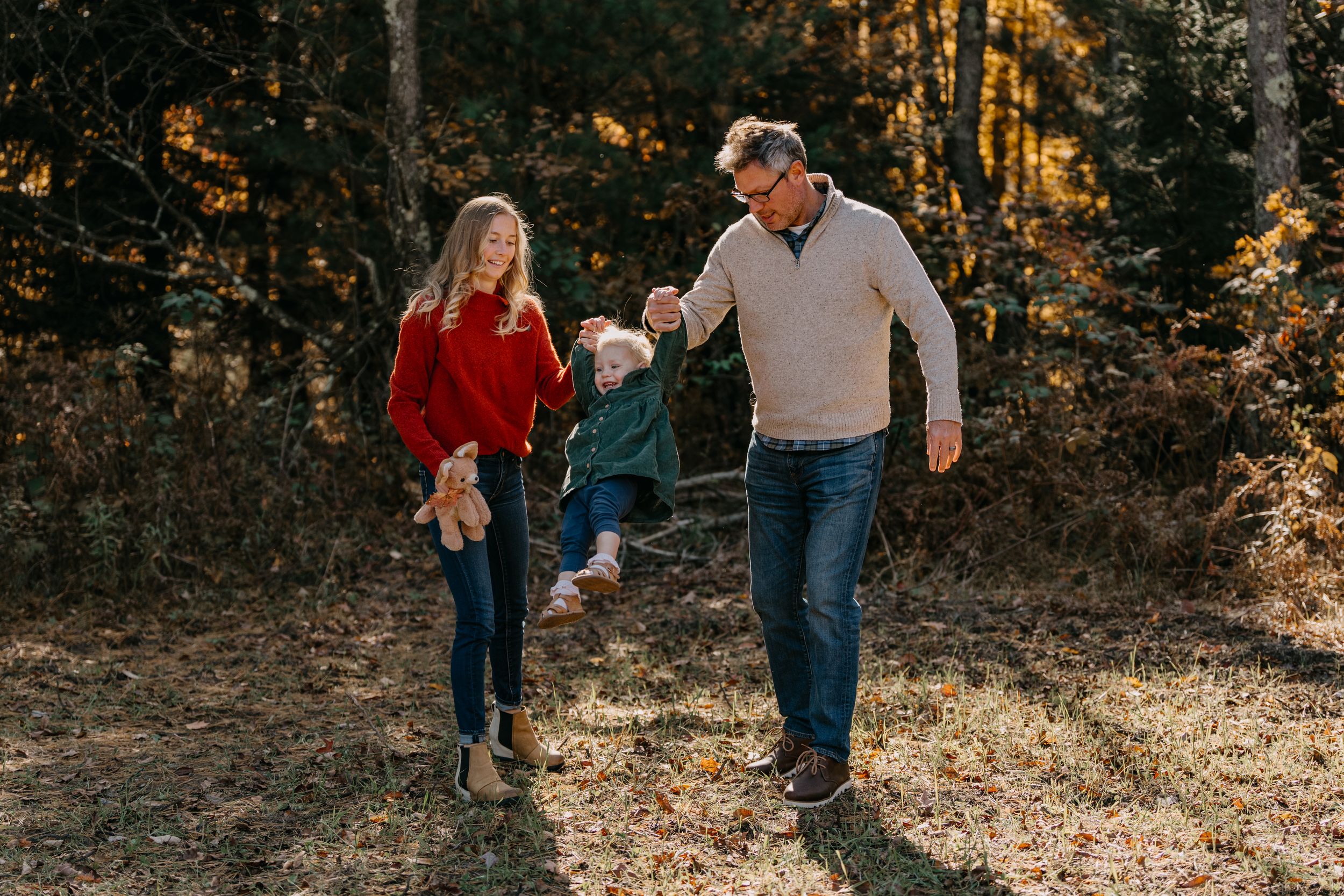 People walk together through an autumn forest with golden sunlight filtering through the trees.