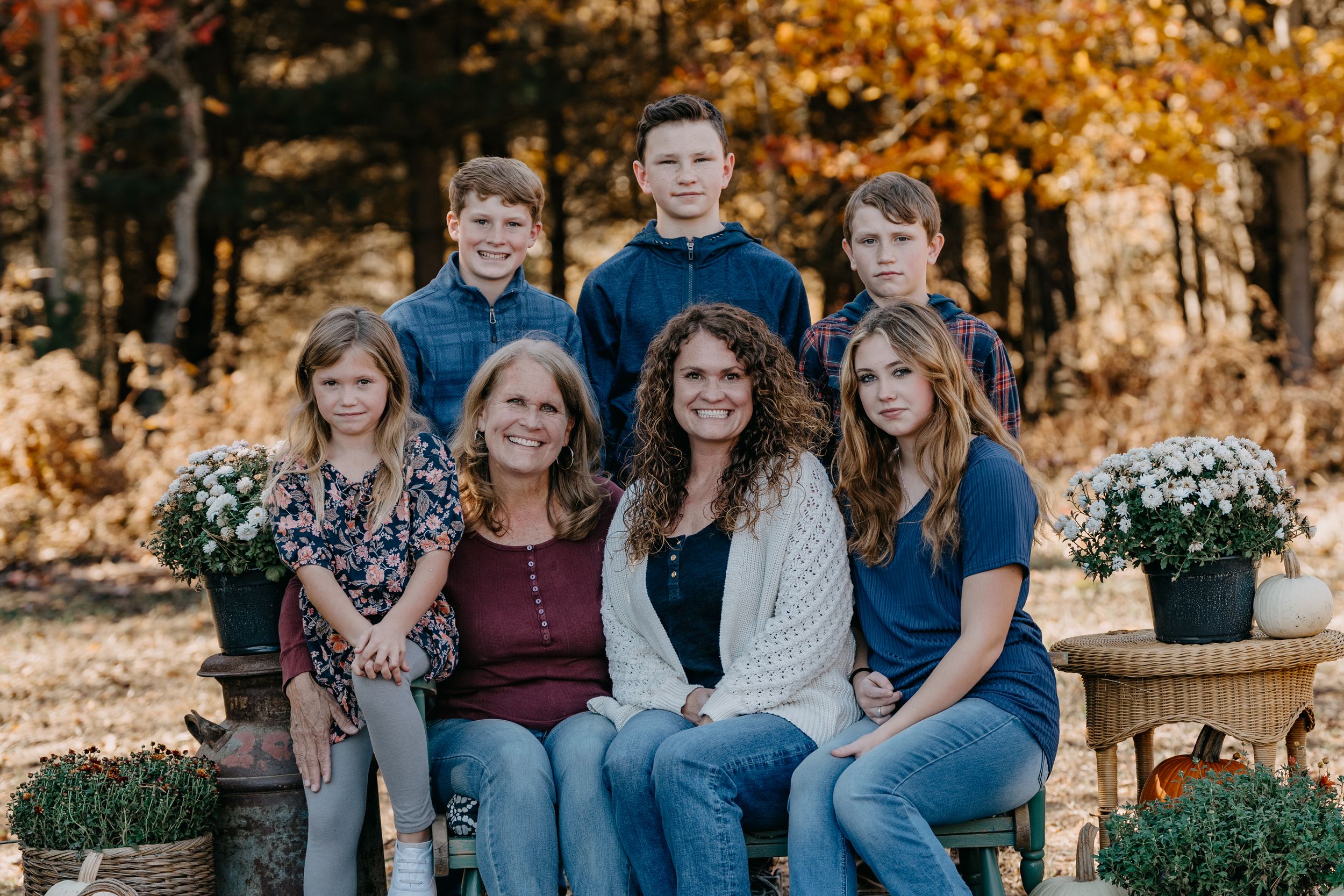Family gathered on rustic wooden bench surrounded by fall foliage and decorative pumpkins.