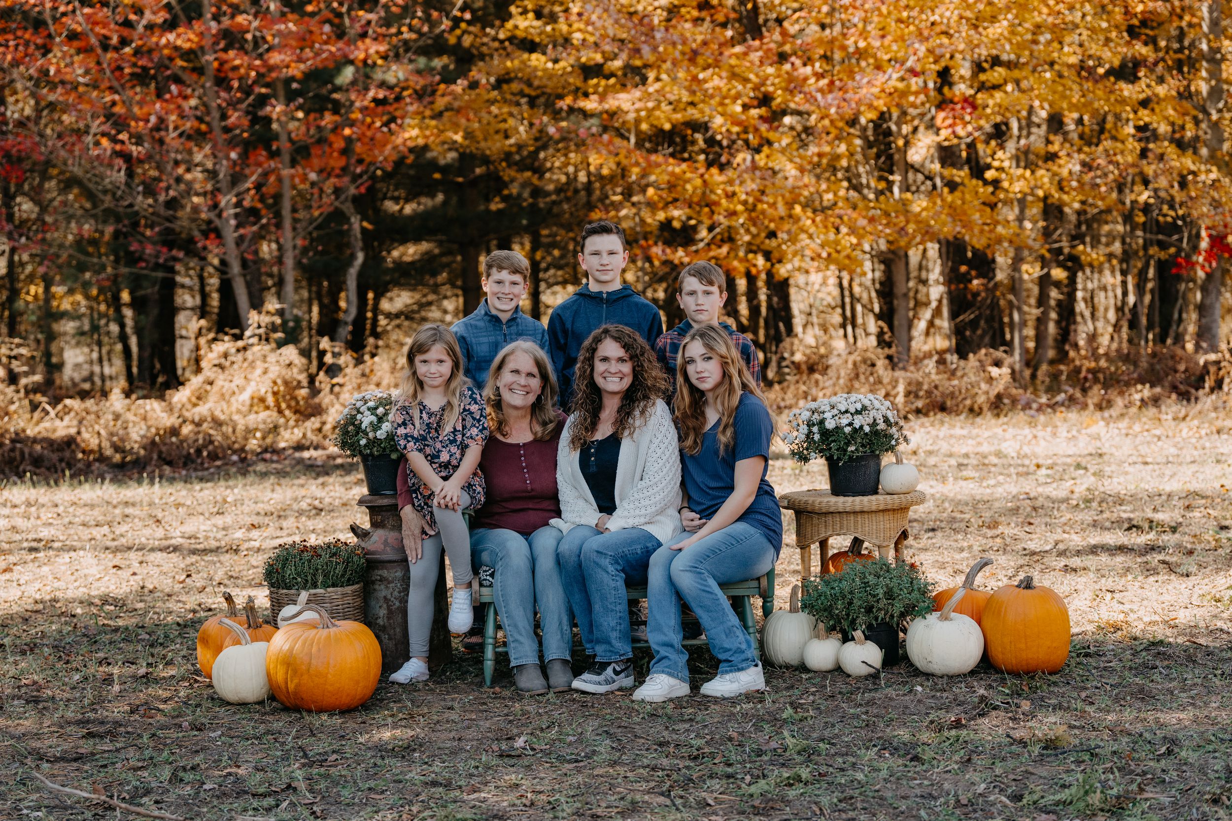 Group seated outdoors with pumpkins and fall foliage creating a cozy autumn family scene.