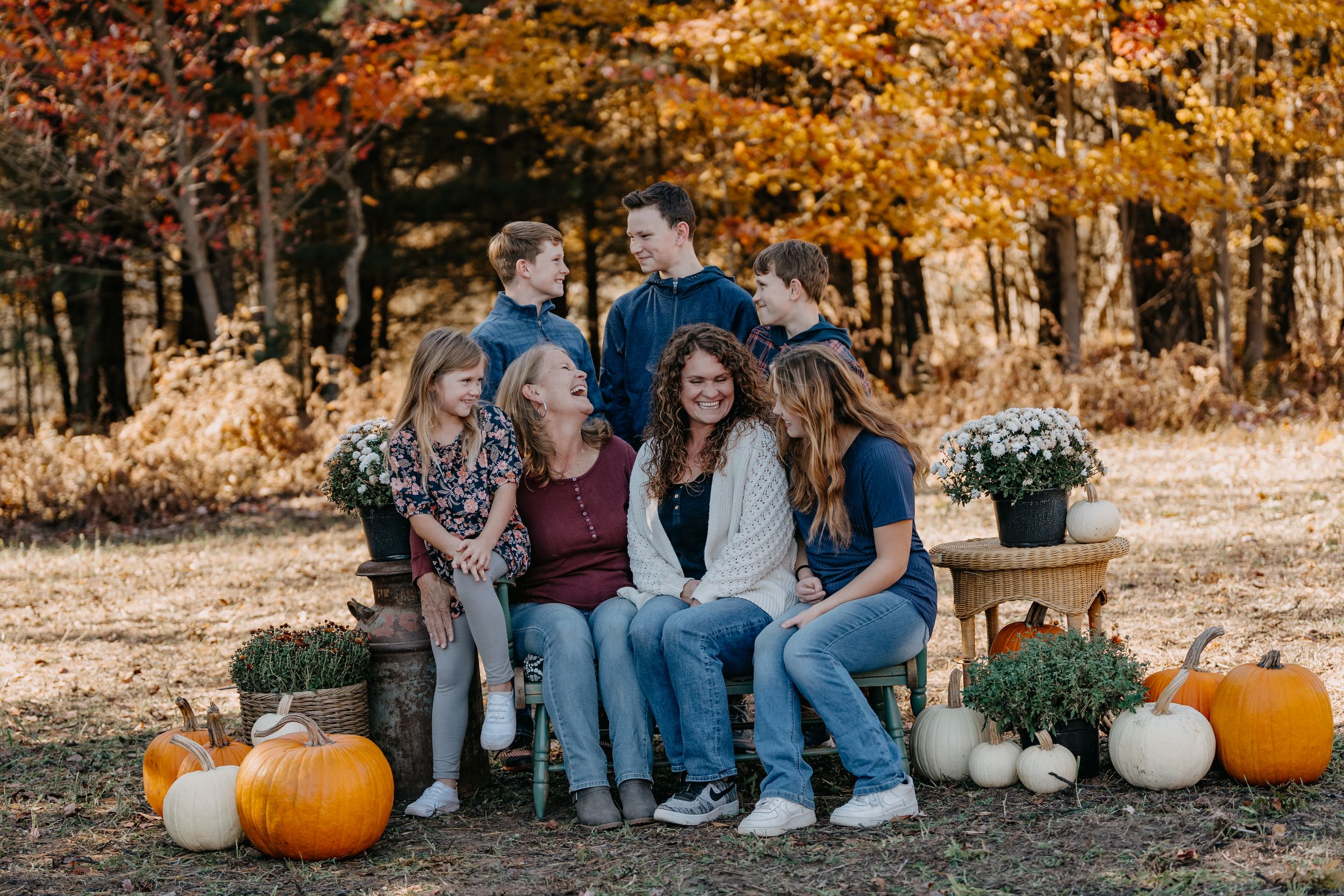Group seated on rustic bench surrounded by orange pumpkins and autumn decor during golden hour.