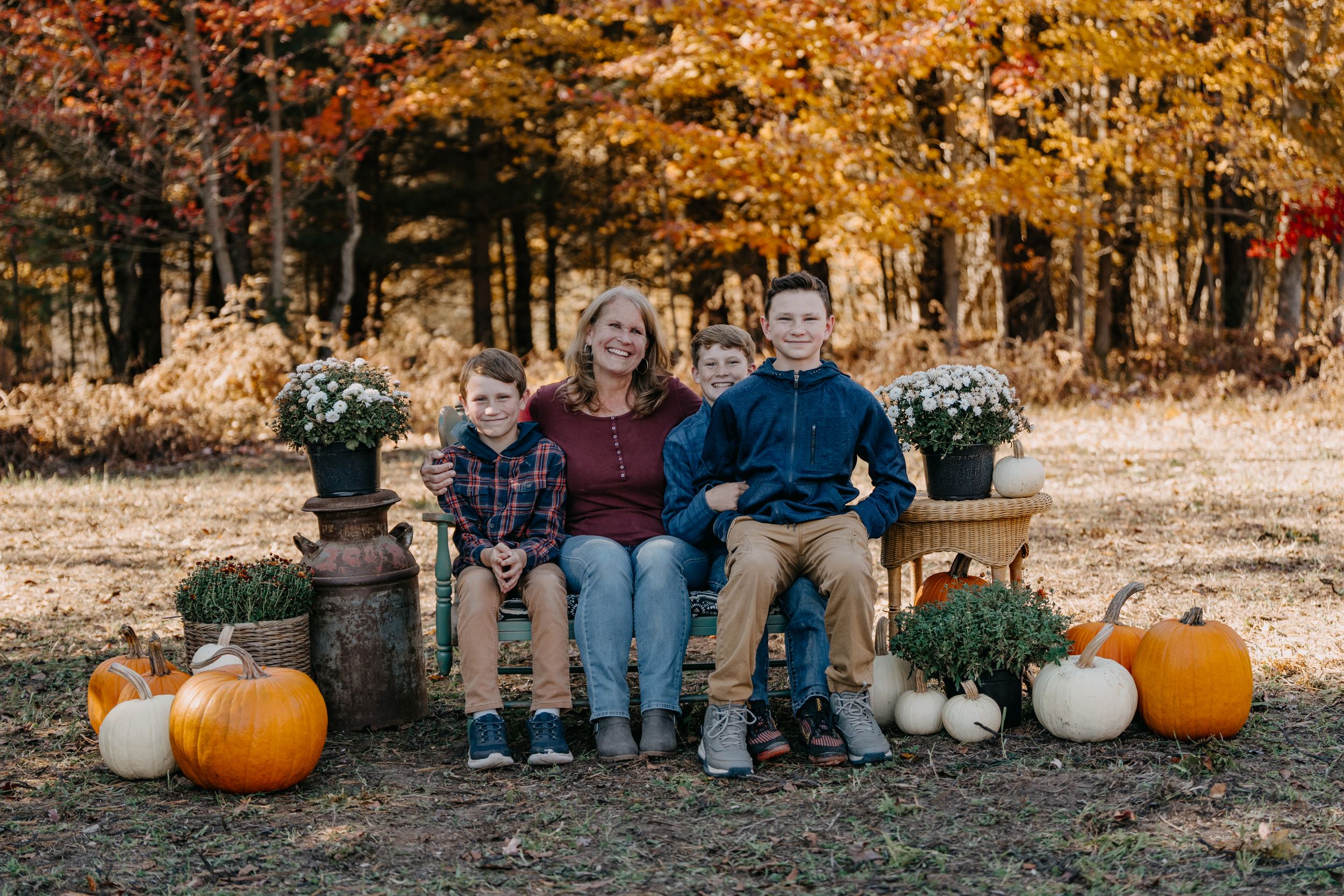 Group enjoying a fall photoshoot with orange leaves and pumpkin decorations in a forest setting.