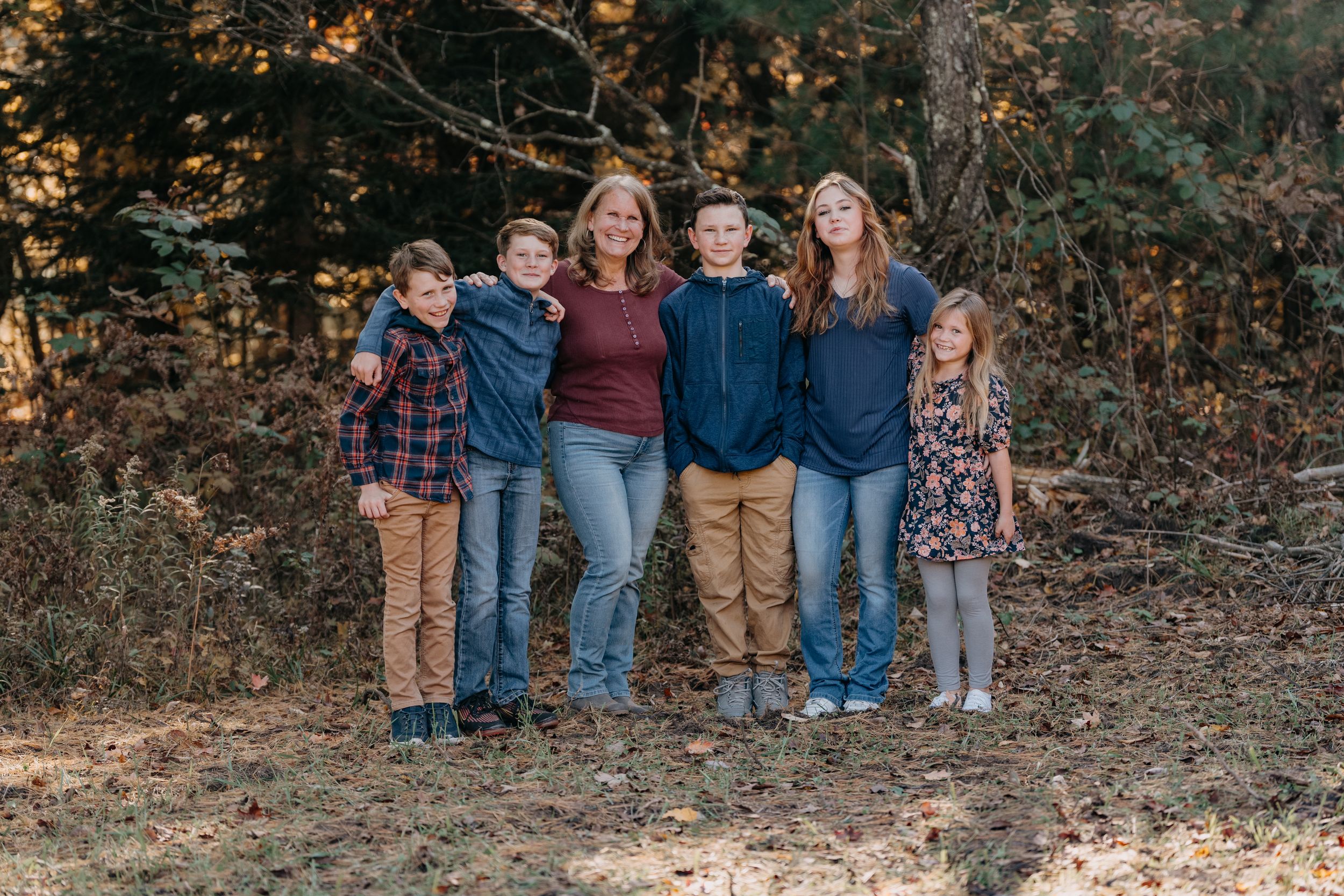 Group gathered for a fall photo outdoors with autumn trees and foliage in background.