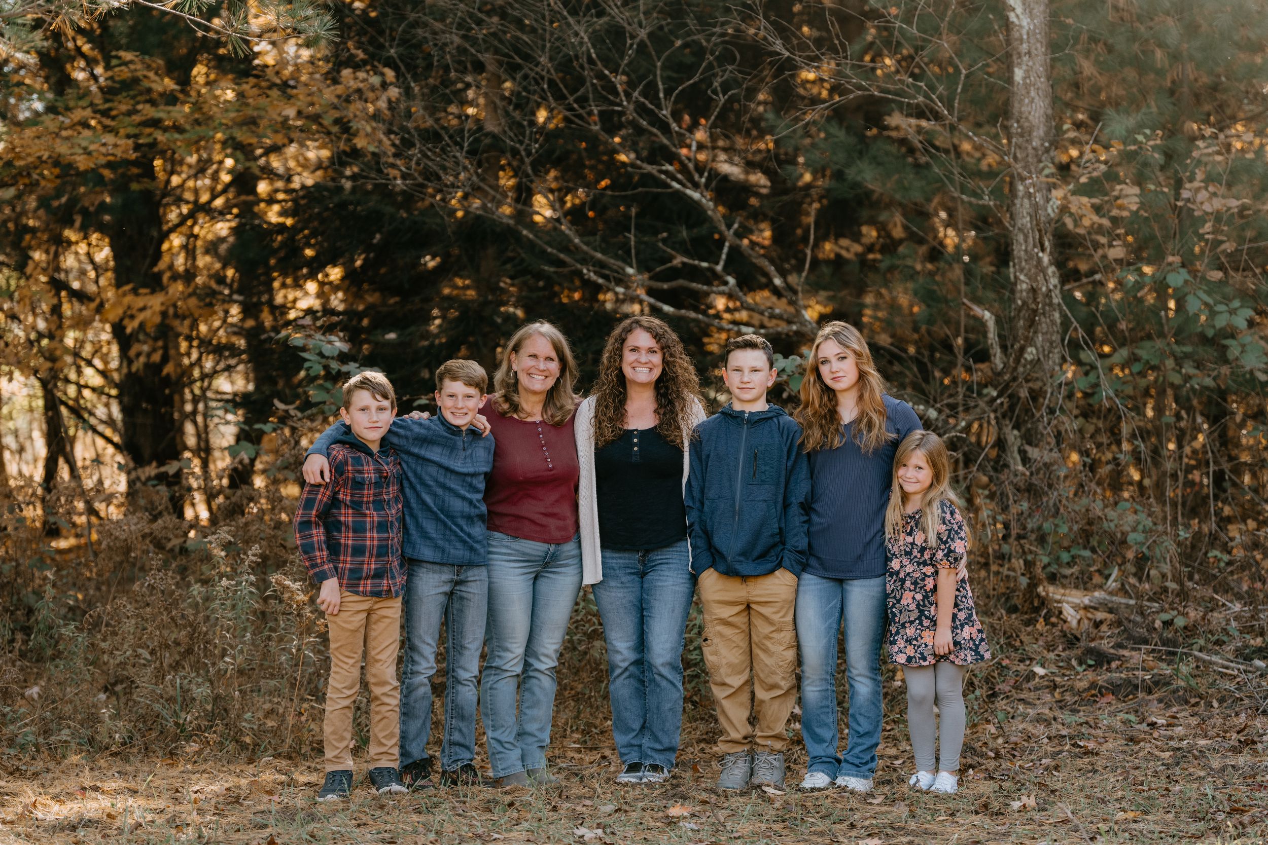 Family group standing together outdoors against autumn trees with golden leaves in natural lighting.