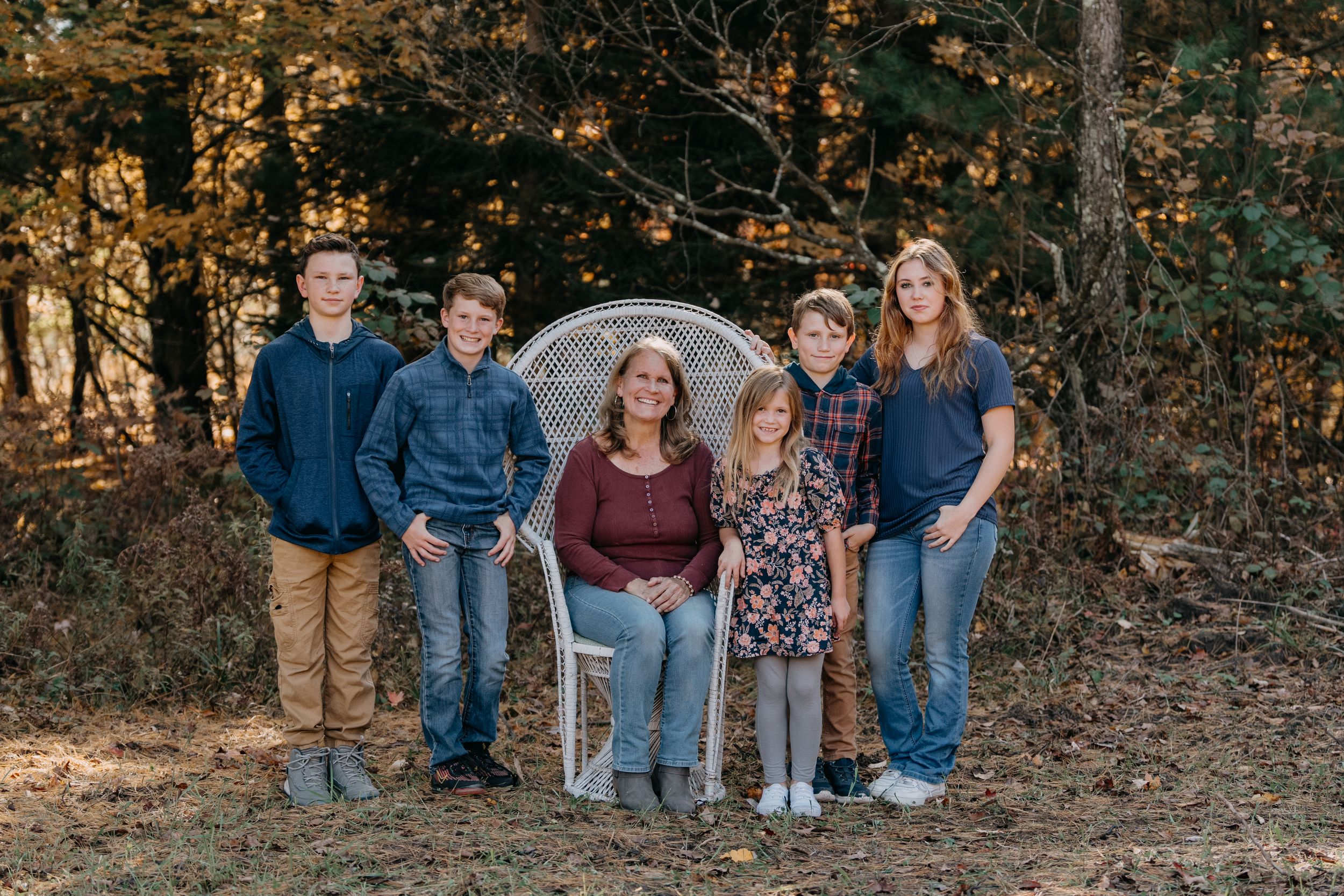 A group of people poses together outdoors in casual attire against a wooded autumn backdrop.