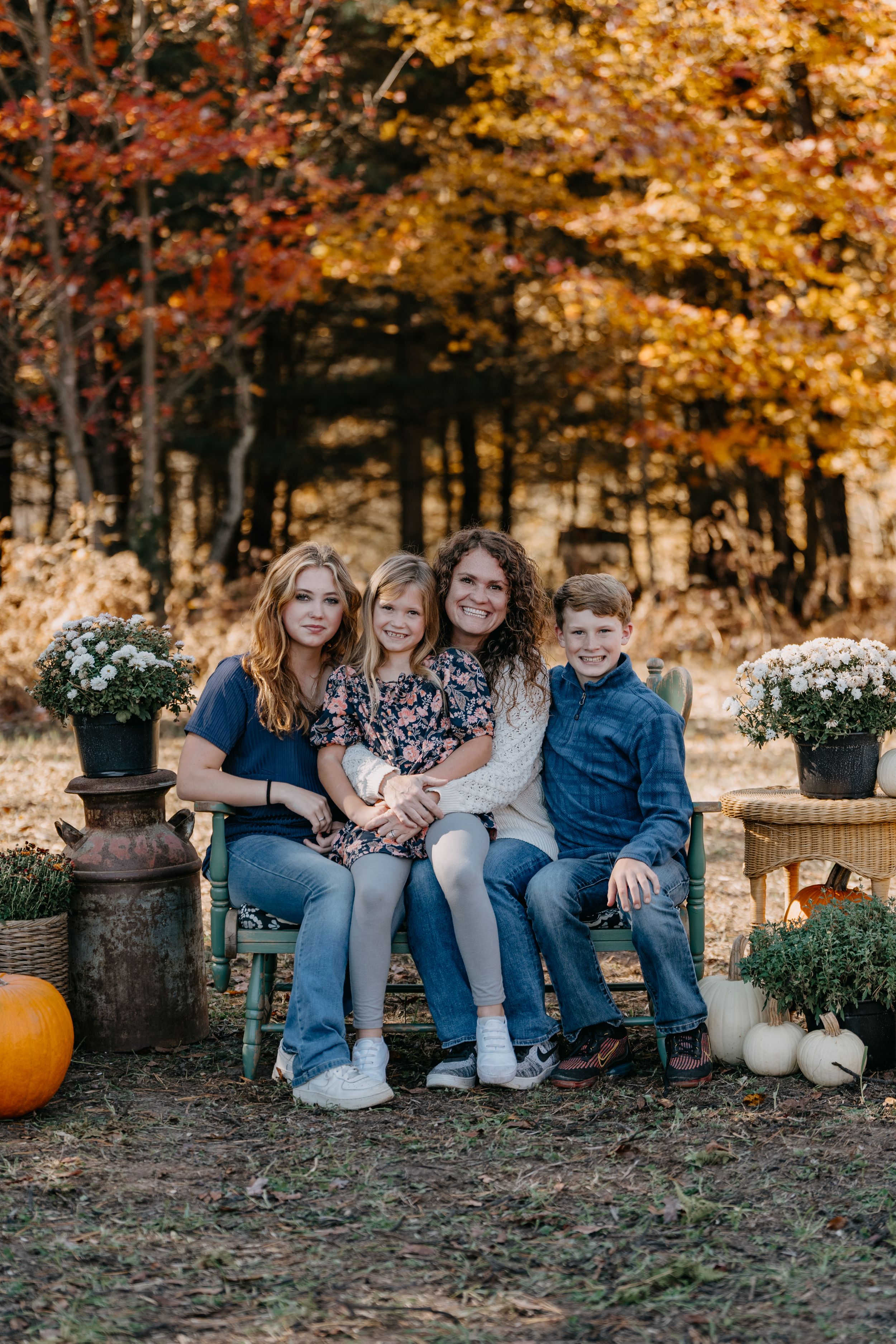 A fall family photo setting with autumn foliage, decorative pumpkins and mums in rustic planters.