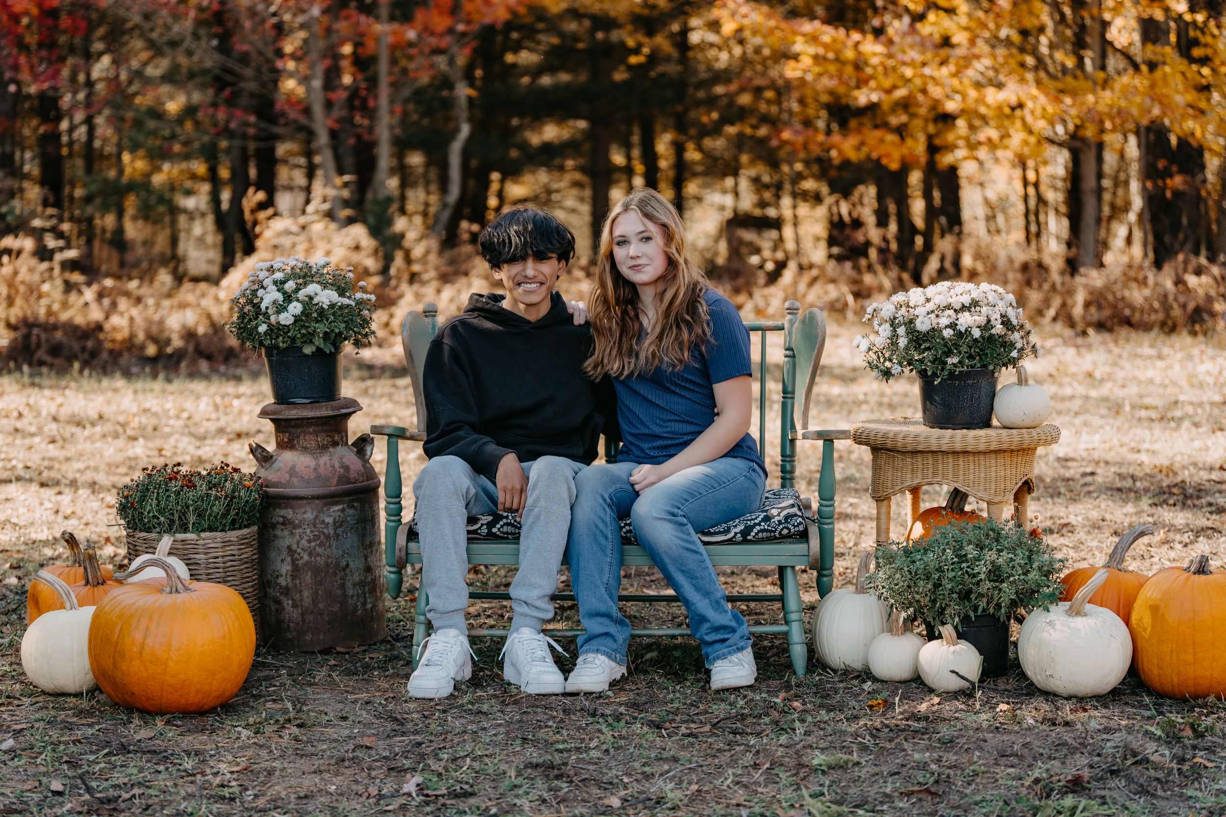 Autumn outdoor scene with rustic bench, pumpkins and white gourds among fall foliage.