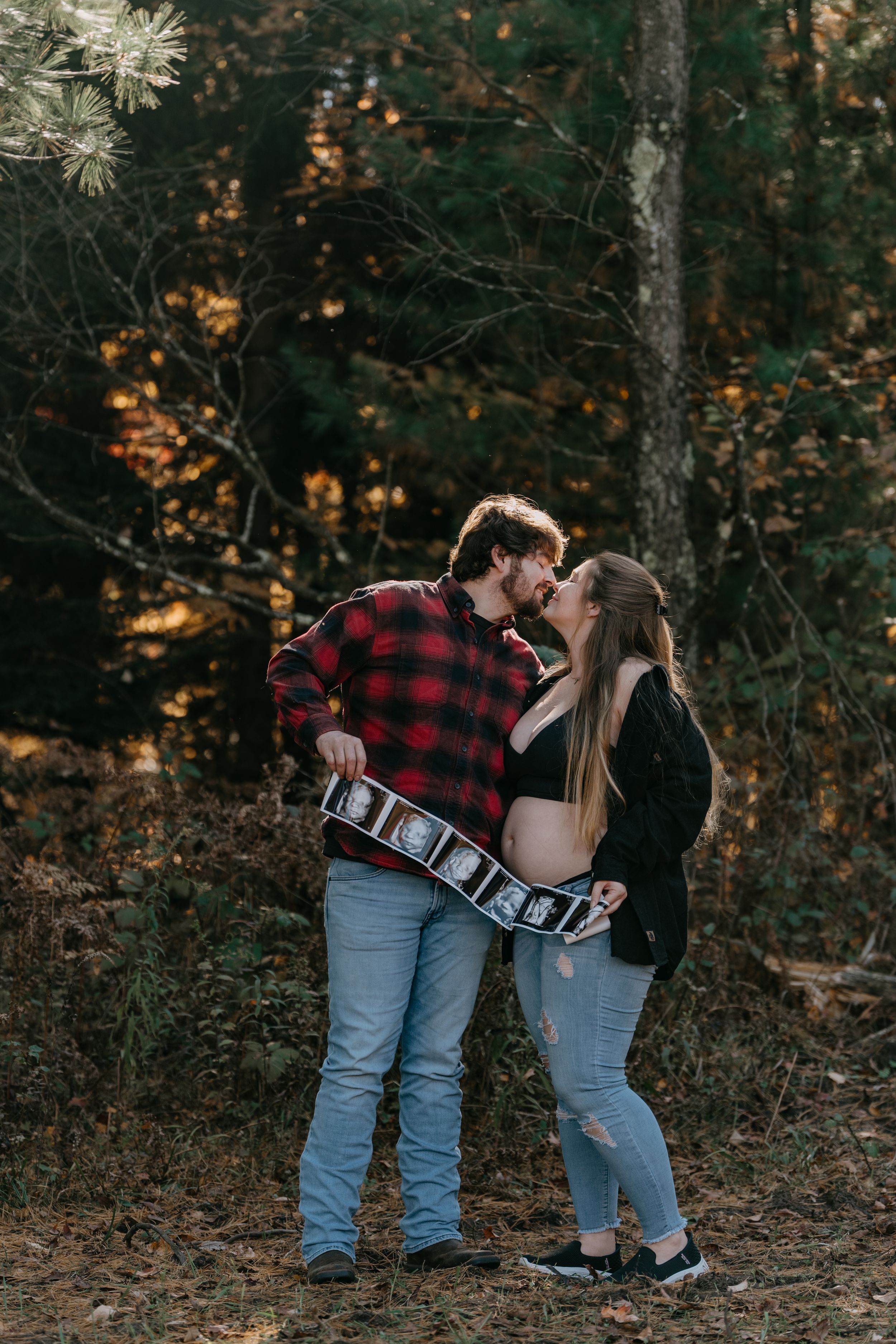 A romantic couple shares a tender moment while holding letter blocks in a forest setting.