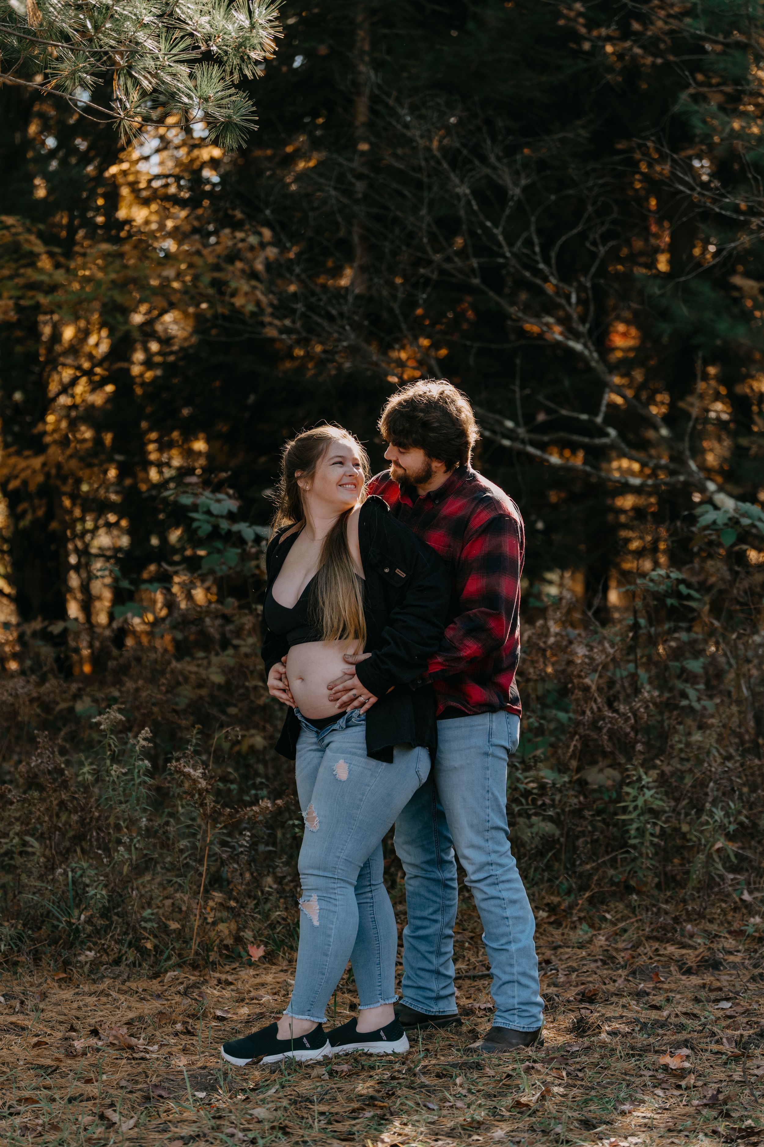 A couple embraces in a wooded area during a romantic autumn photoshoot wearing casual attire.