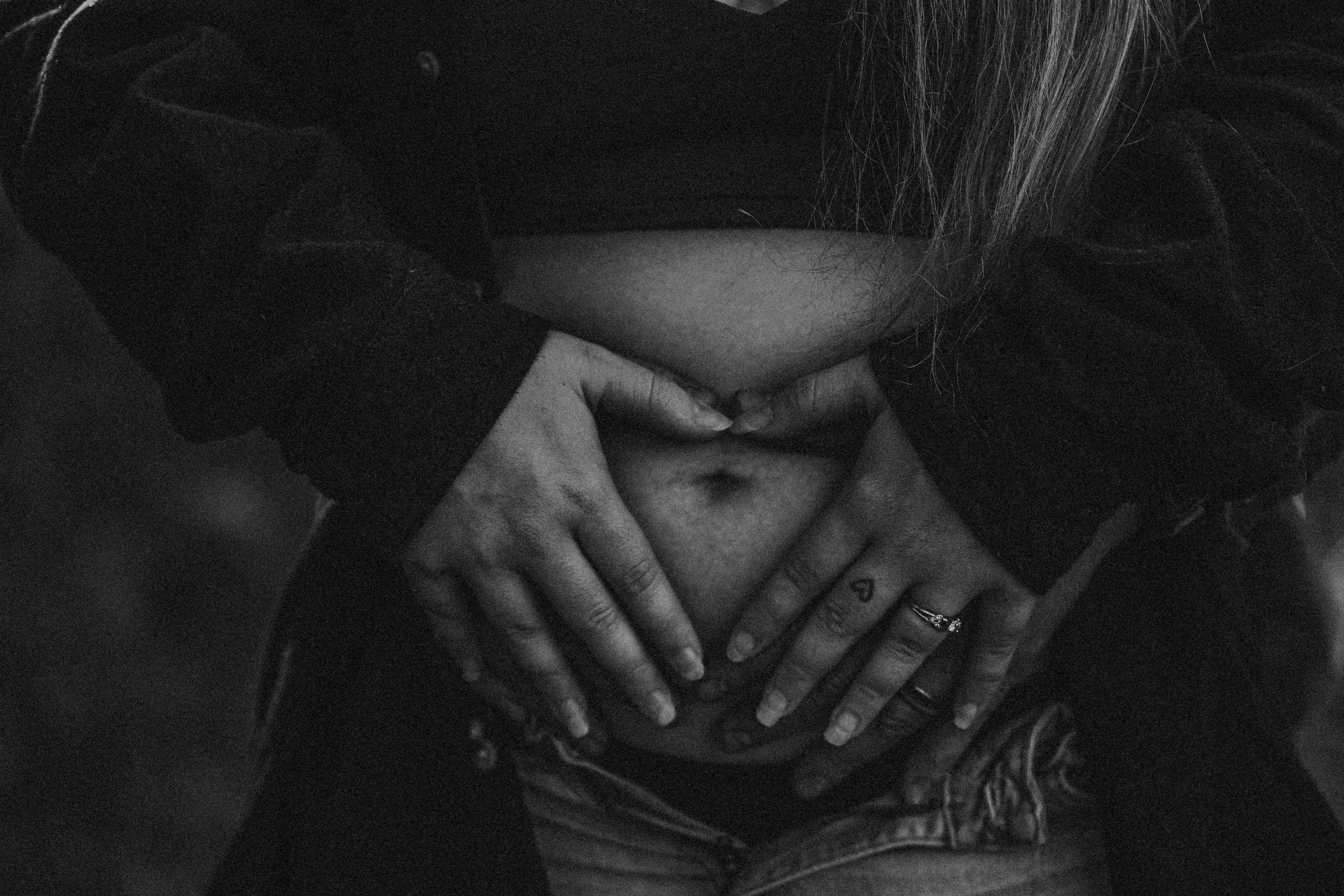 Close-up shots of hands gently resting on pregnant belly in black and white.