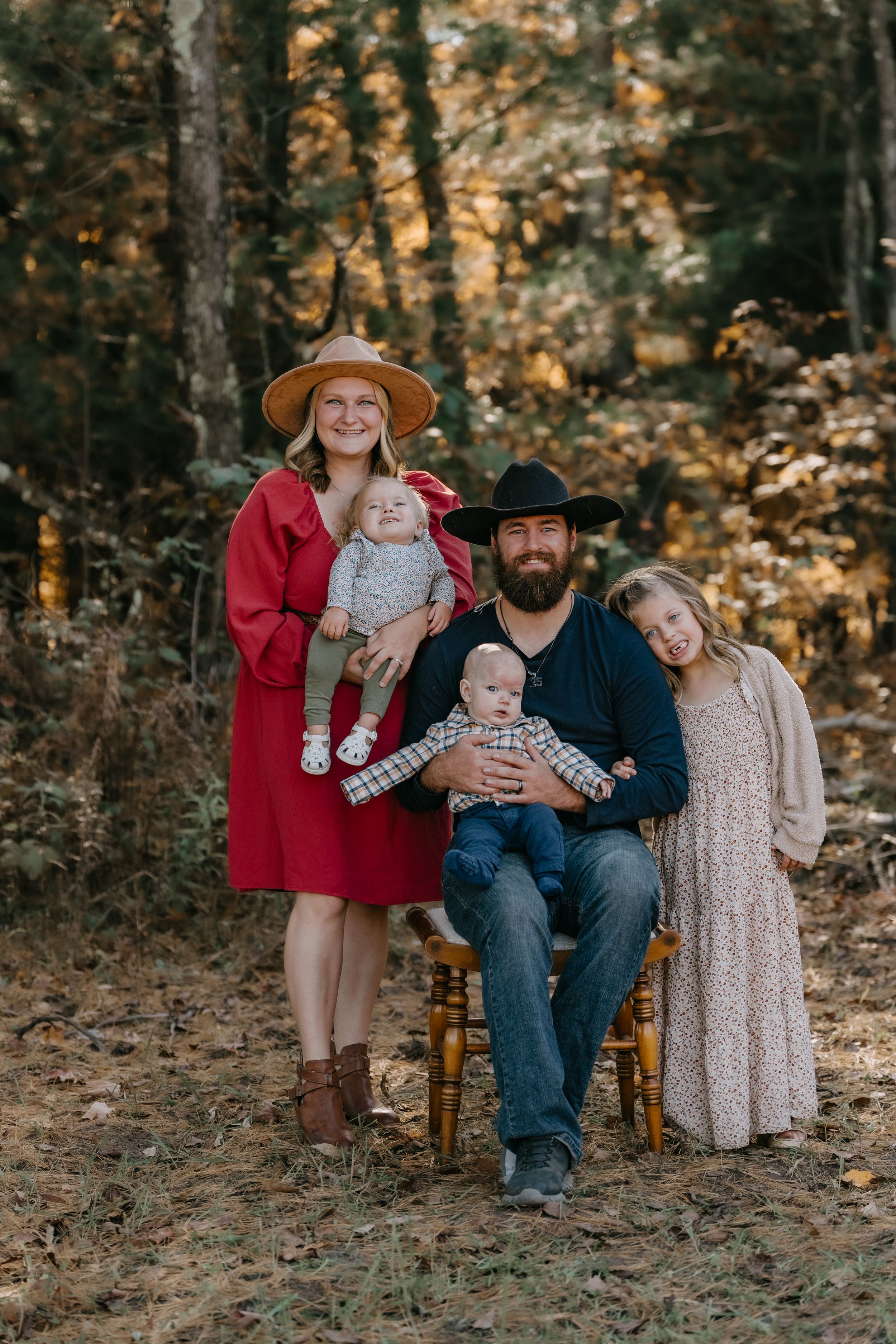 A family sits together on wooden chairs in a warm autumn forest setting.