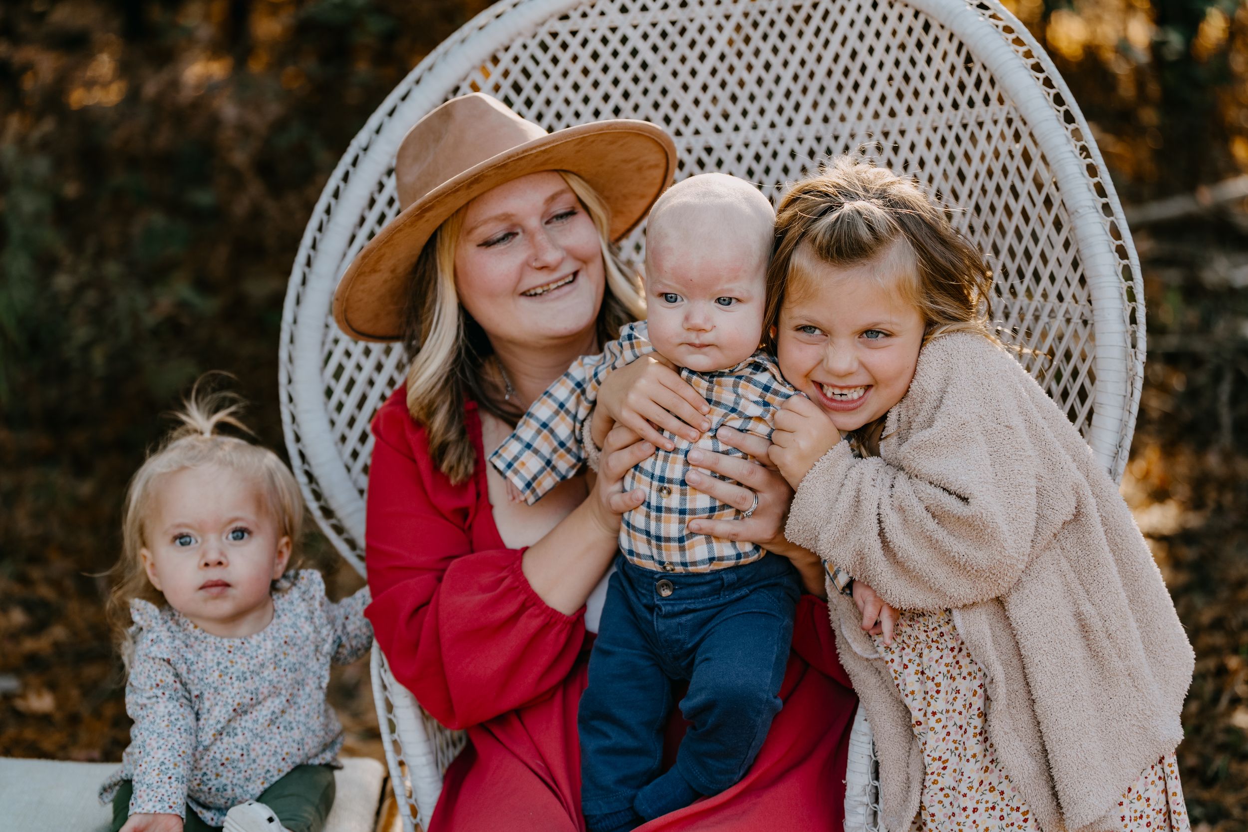 A white wicker peacock chair with a family posing against an autumn forest backdrop.