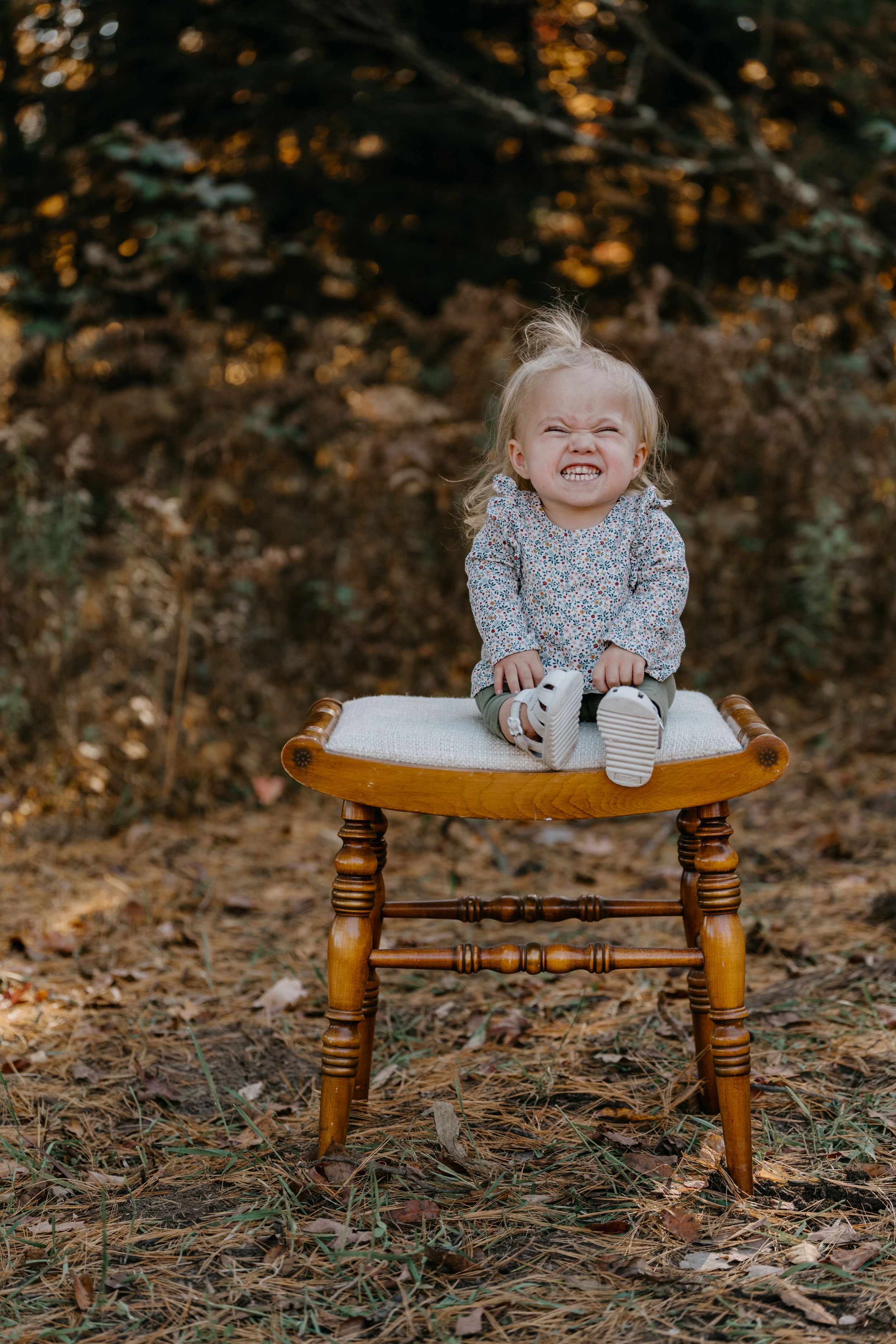 A child playfully sits on a rustic wooden bench surrounded by fallen autumn leaves.