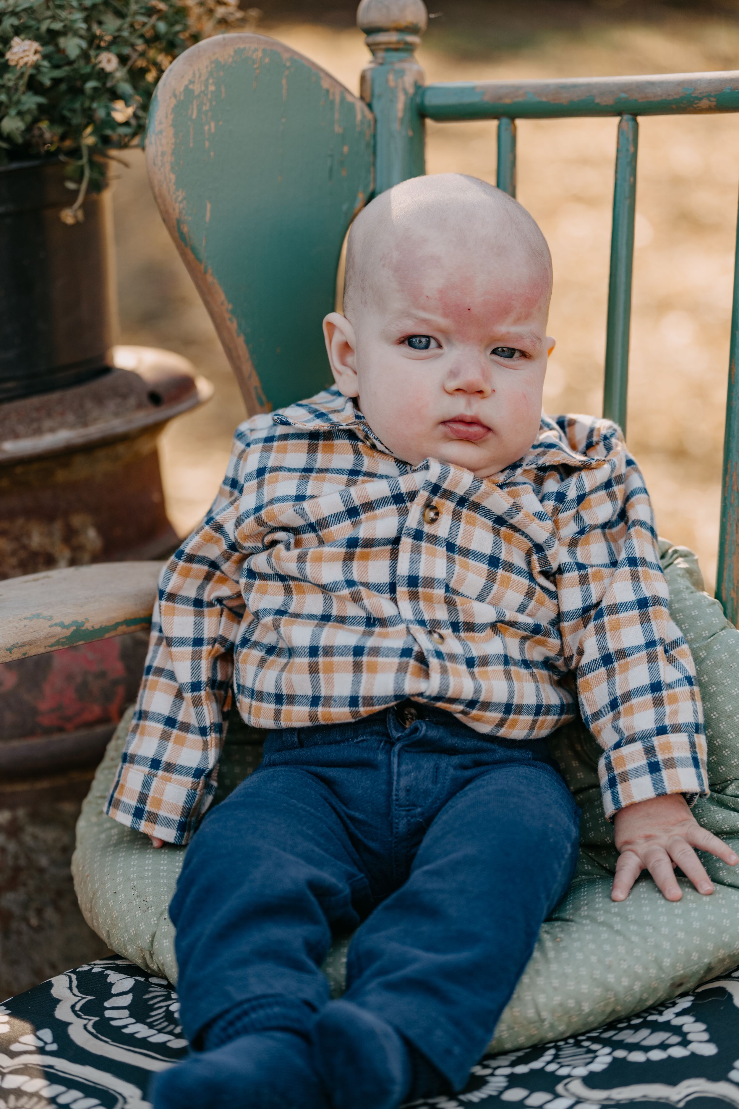 Young child in plaid shirt and jeans sits on vintage turquoise chair with patterned blanket.