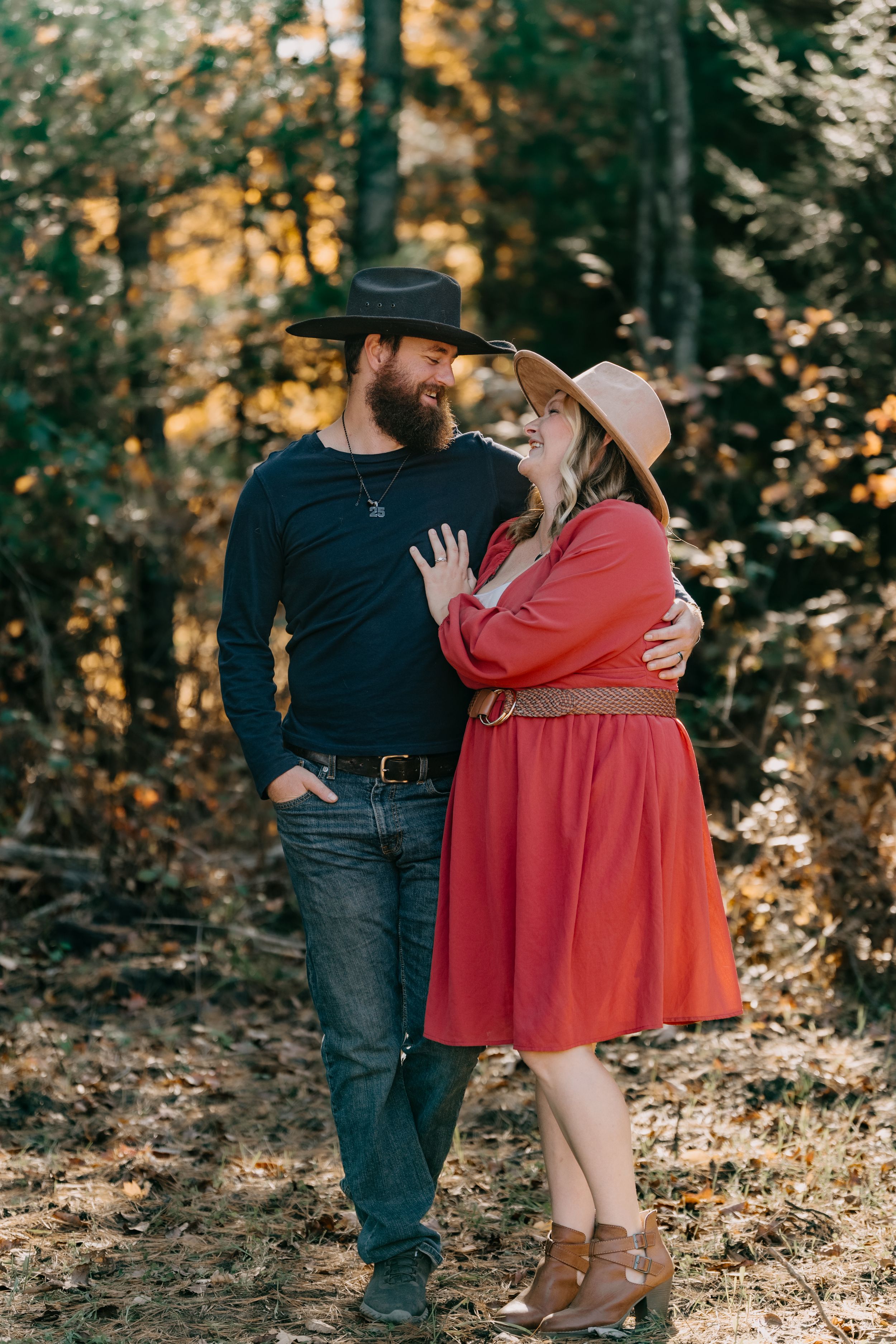 Couple in casual western attire sharing romantic moment in sunlit forest setting.