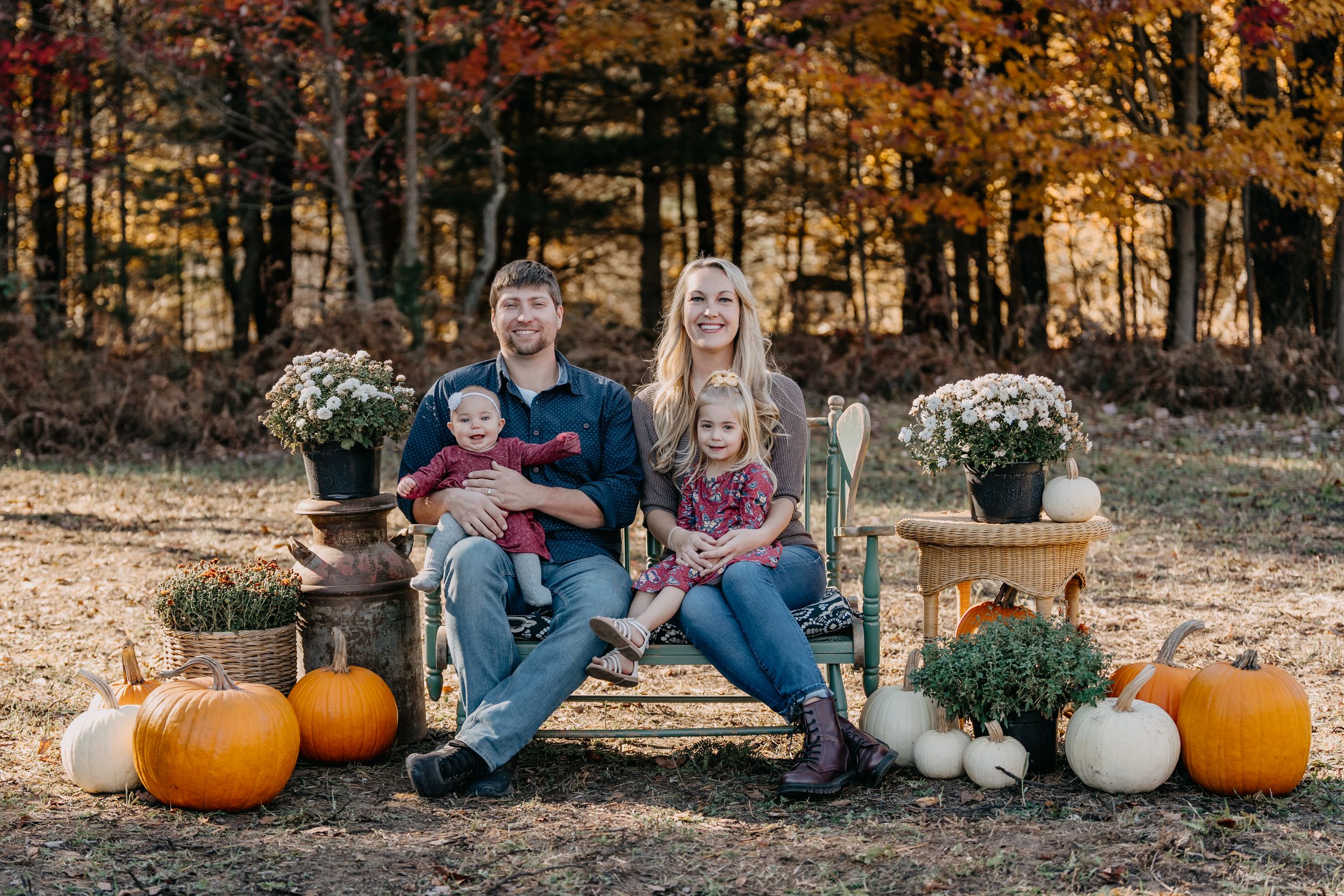 Rustic fall outdoor scene with family sitting on bench among pumpkins and potted chrysanthemums at sunset.