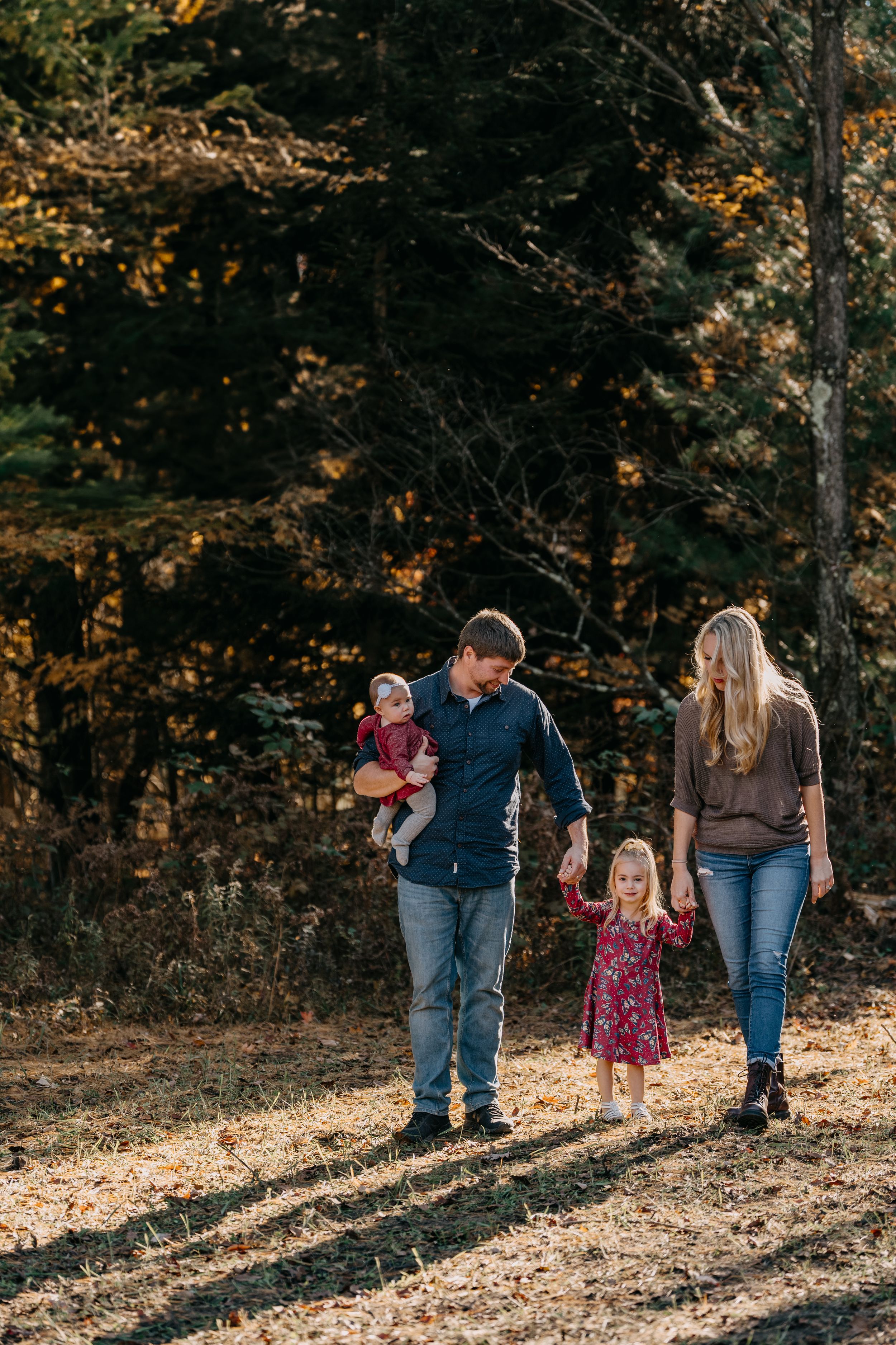 A family holding hands walks together through an autumn forest path on a sunny afternoon, casting long shadows.