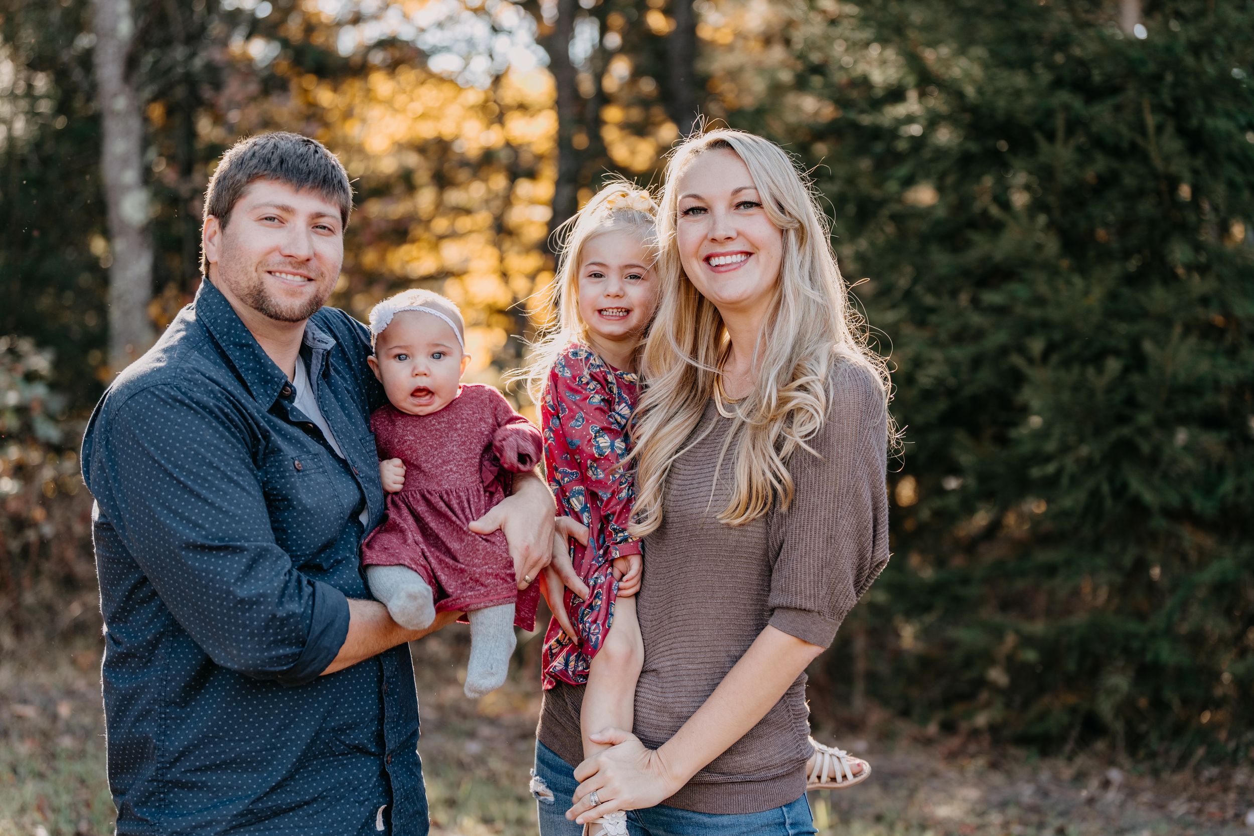 A family portrait captured in warm autumn lighting against a backdrop of fall foliage.