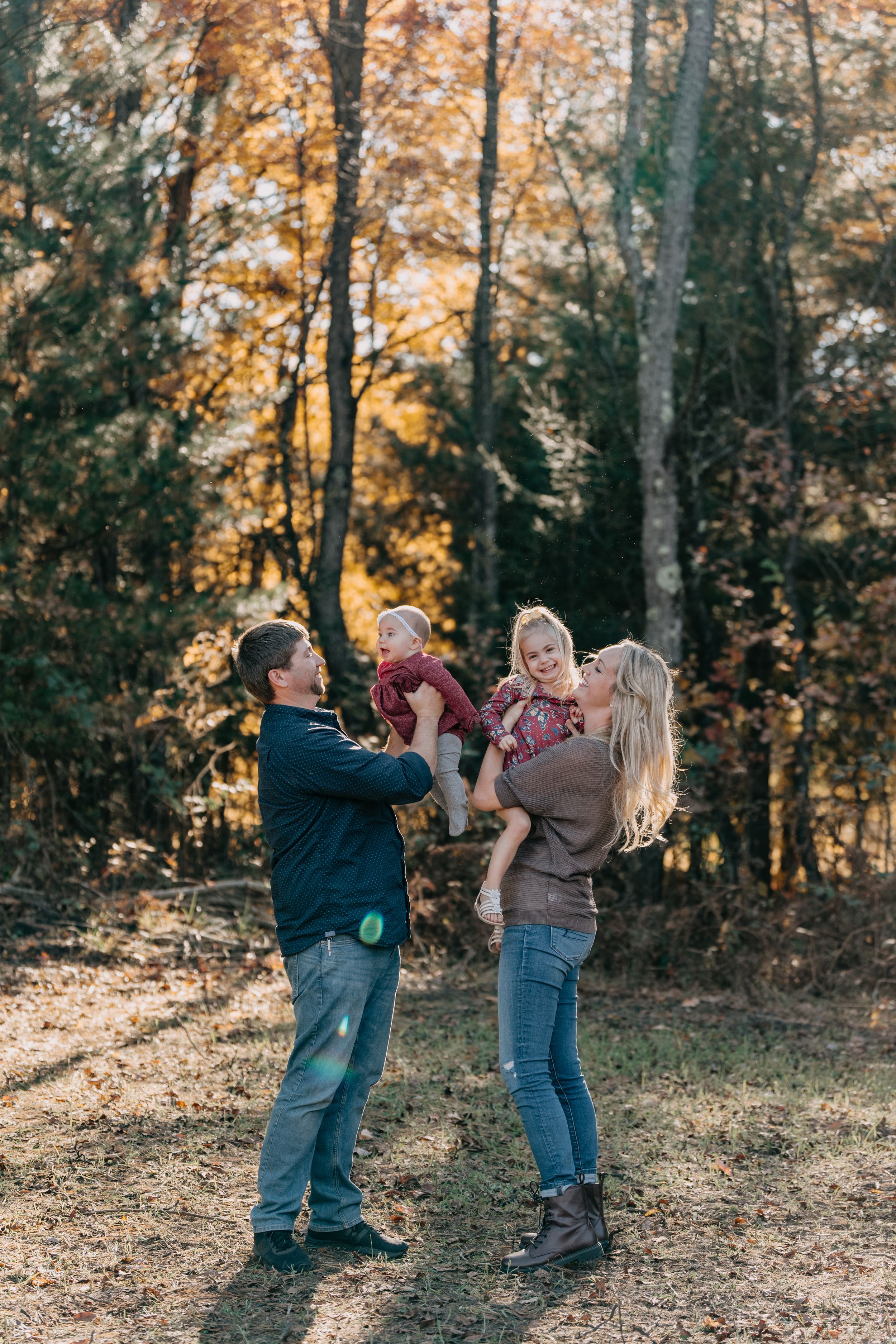 A playful outdoor autumn photoshoot moment captured in front of trees with golden fall colors.
